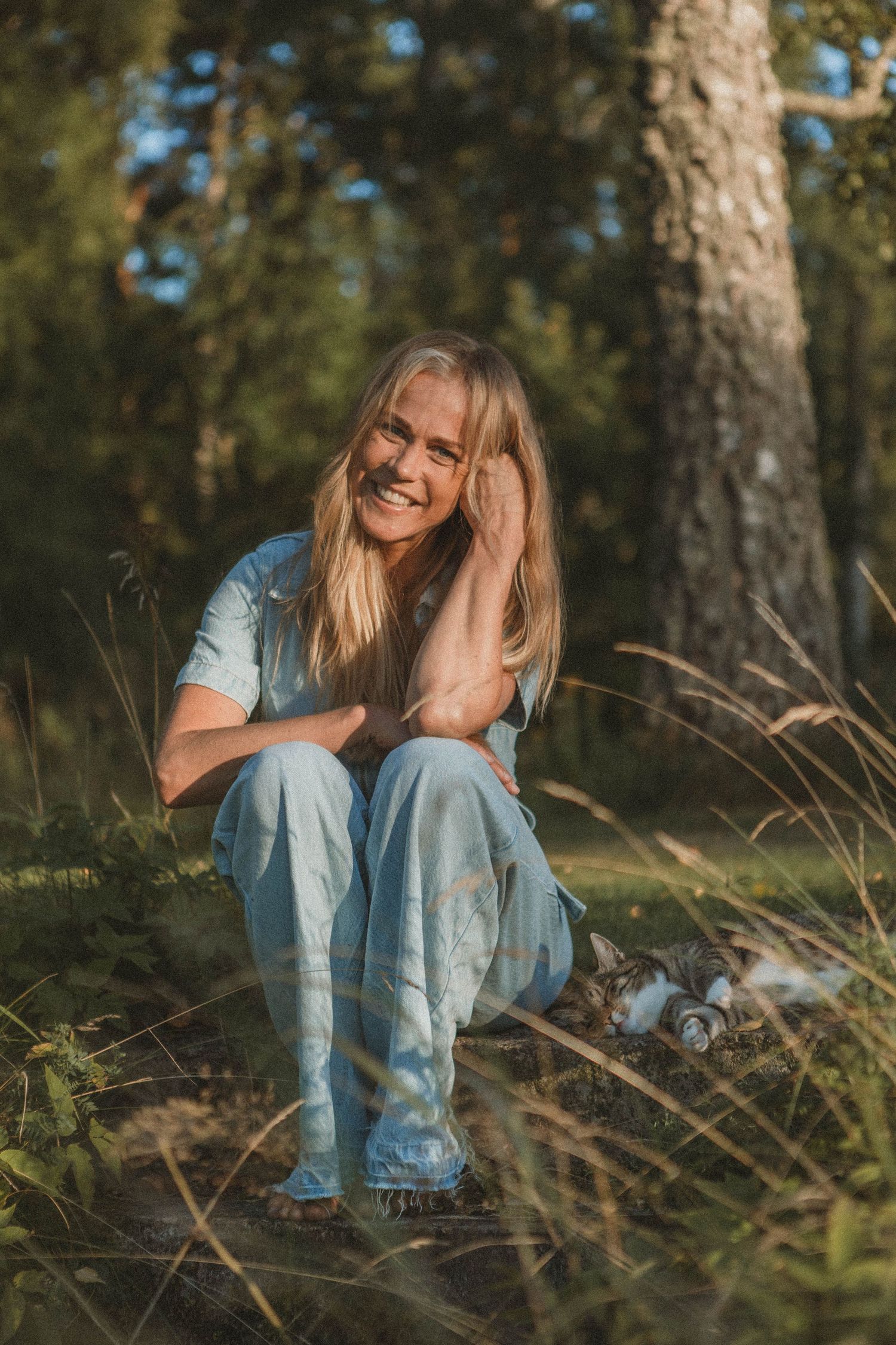 Casual outdoor portrait of someone sitting in denim among pine trees.