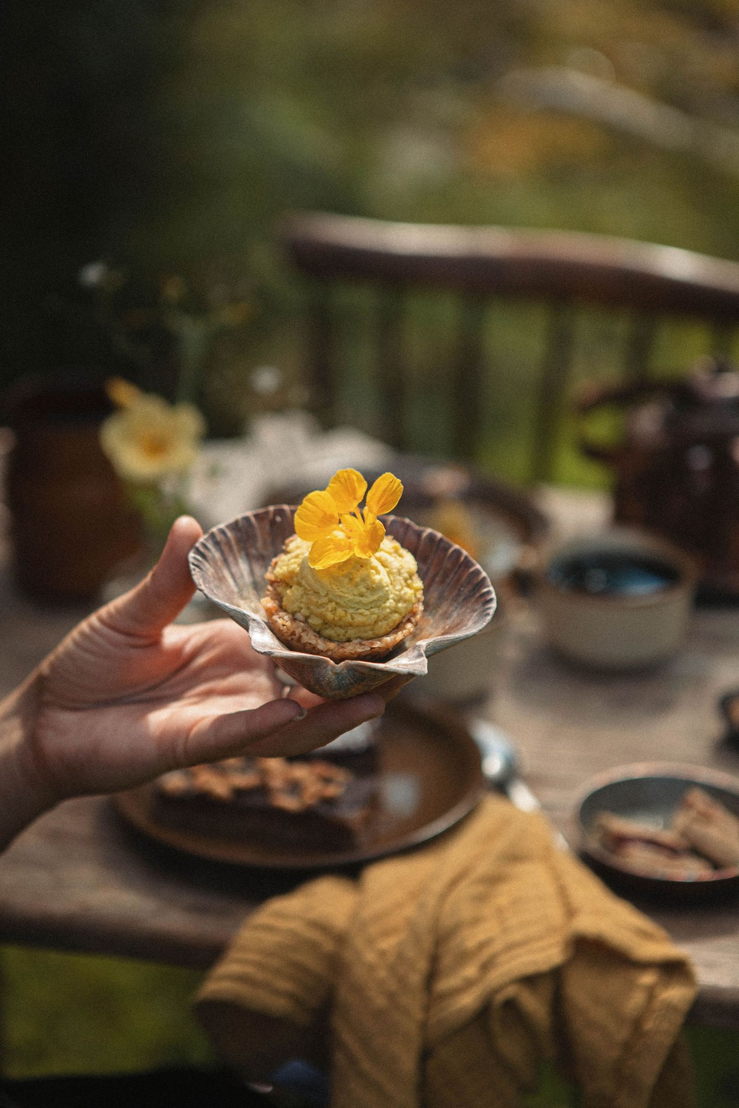 A delicate pastry topped with yellow edible flowers being served on an elegant shell-shaped plate.