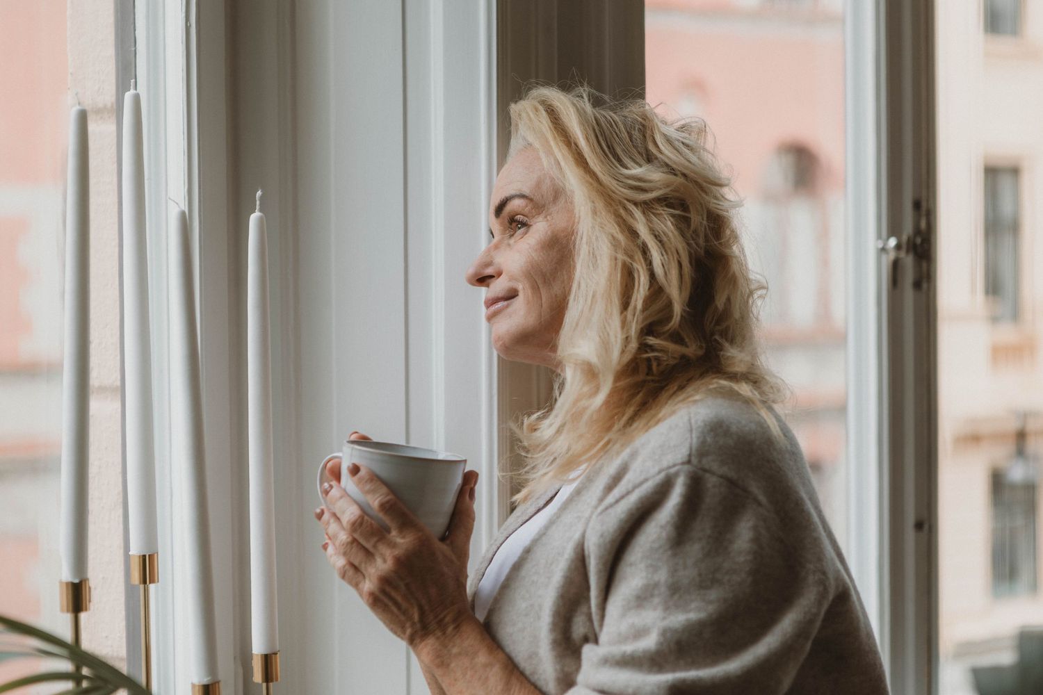 Cozy morning moment by window holding coffee cup with natural smile.