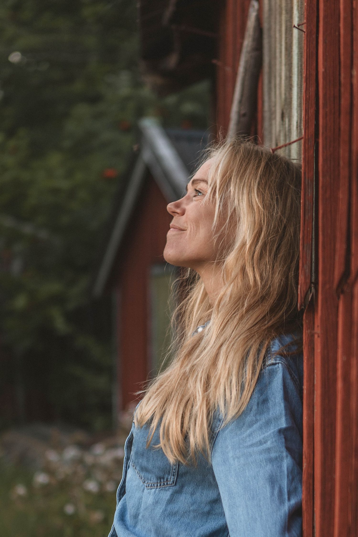 Relaxed pose against red barn wall with eyes closed and blonde hair.