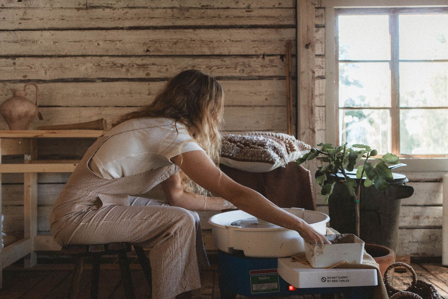 Pottery workshop scene with wheel and tools in a rustic wooden space.