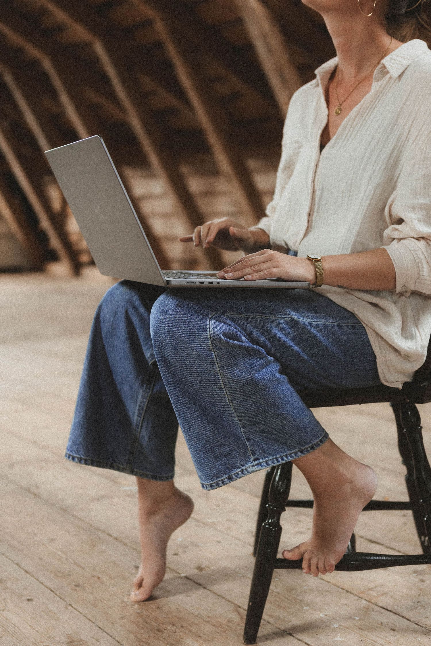 Person sitting on wooden floor wearing casual jeans and white top while working on laptop.