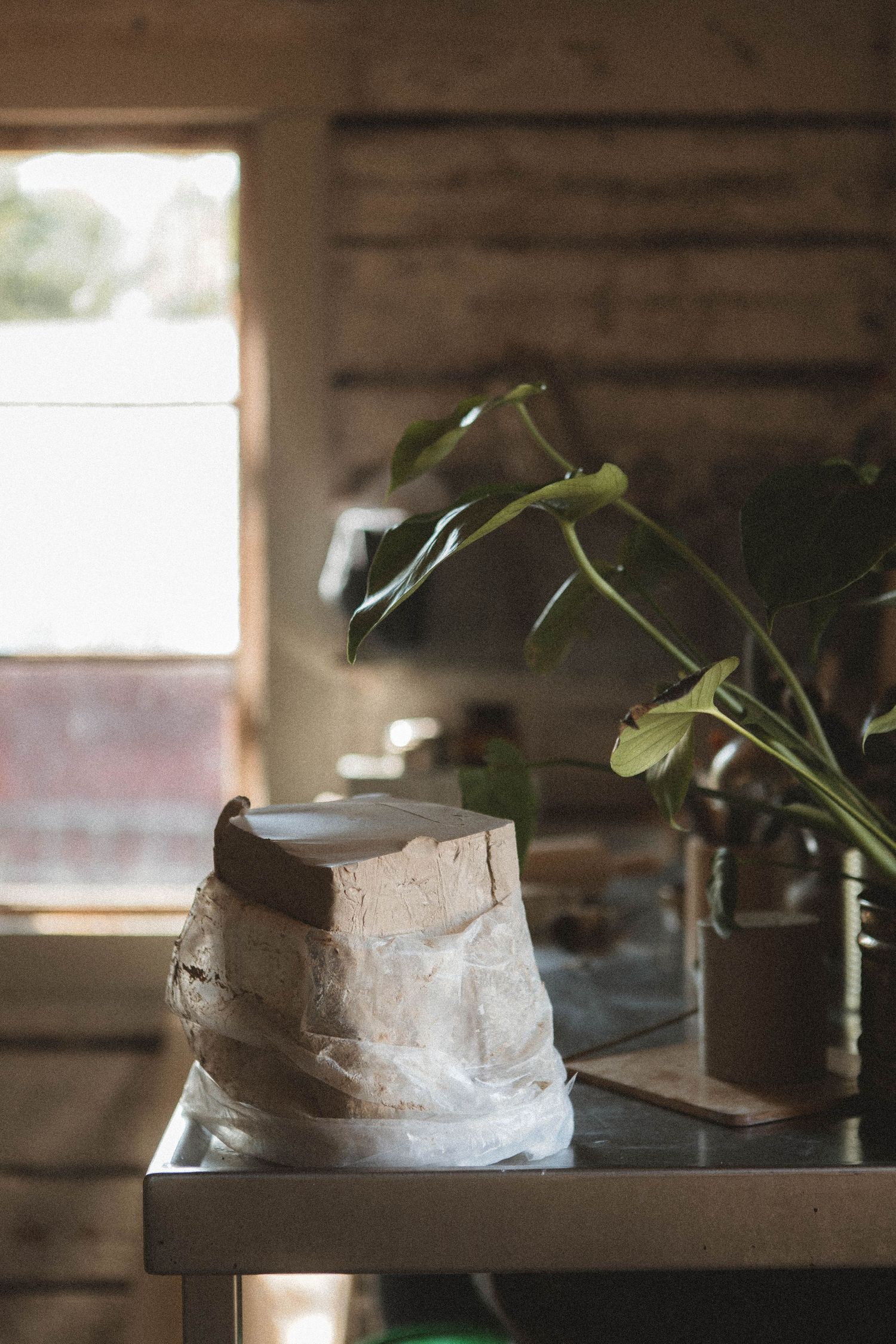 A rustic pottery piece sits on a wooden table near a window with green plants in a cabin setting.