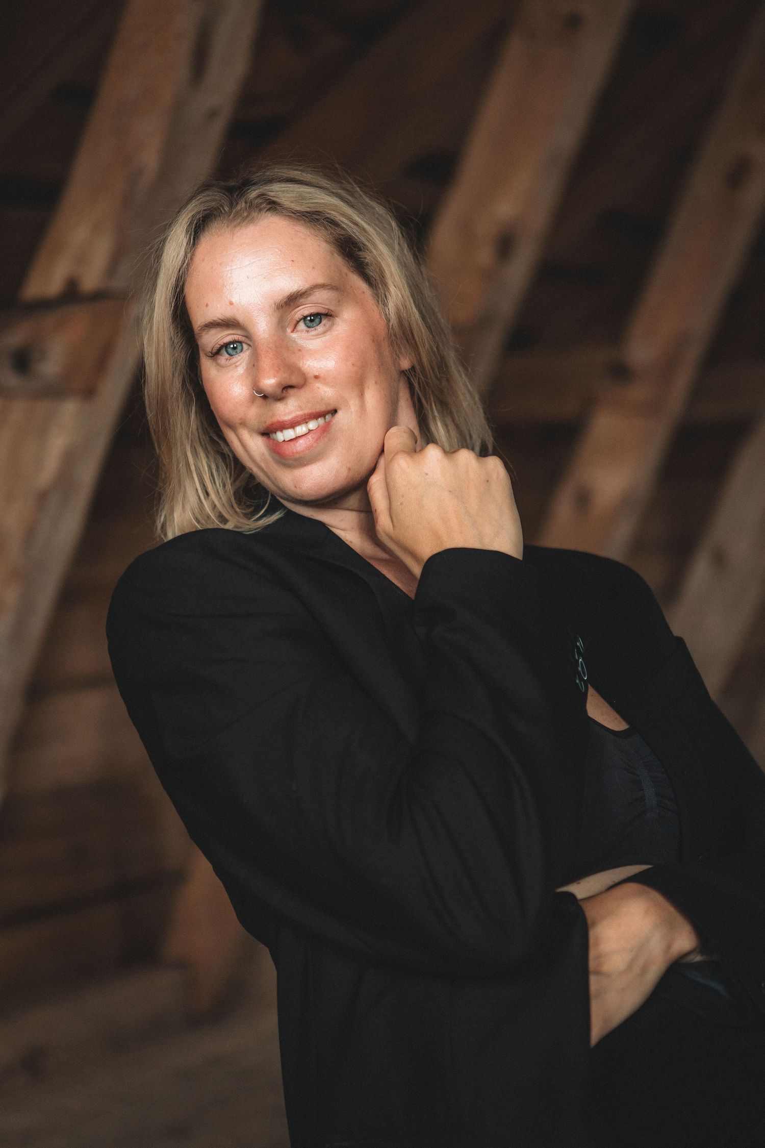 Warm indoor portrait against wooden beams wearing a cozy black sweater.