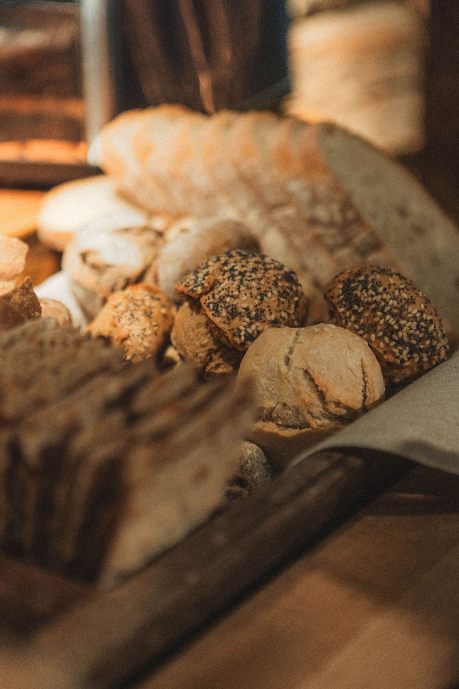 Artisanal bread loaves with various toppings like seeds and grains displayed in warm lighting.