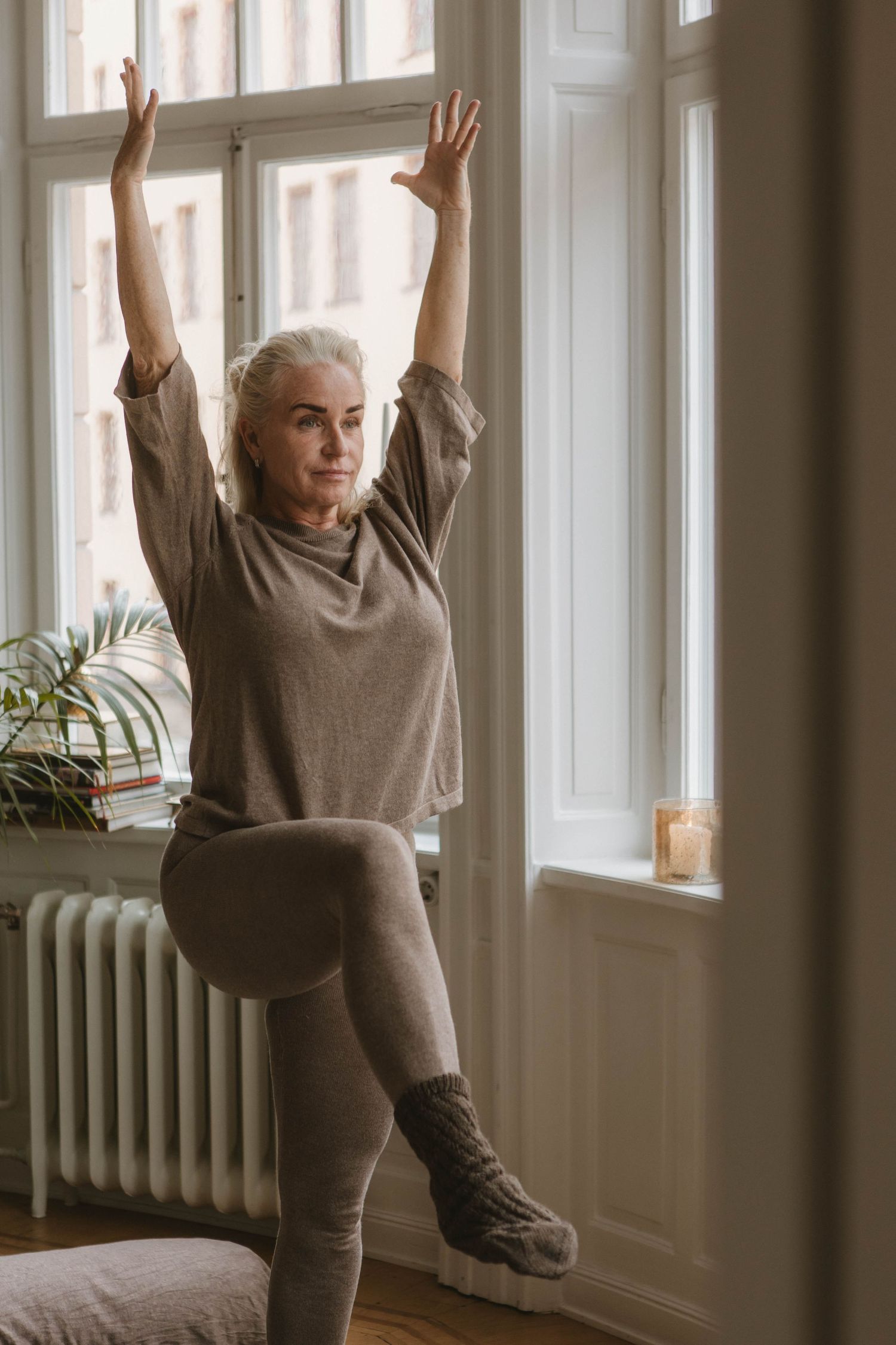 Person stretches and exercises near a sunny window while wearing comfortable loungewear.