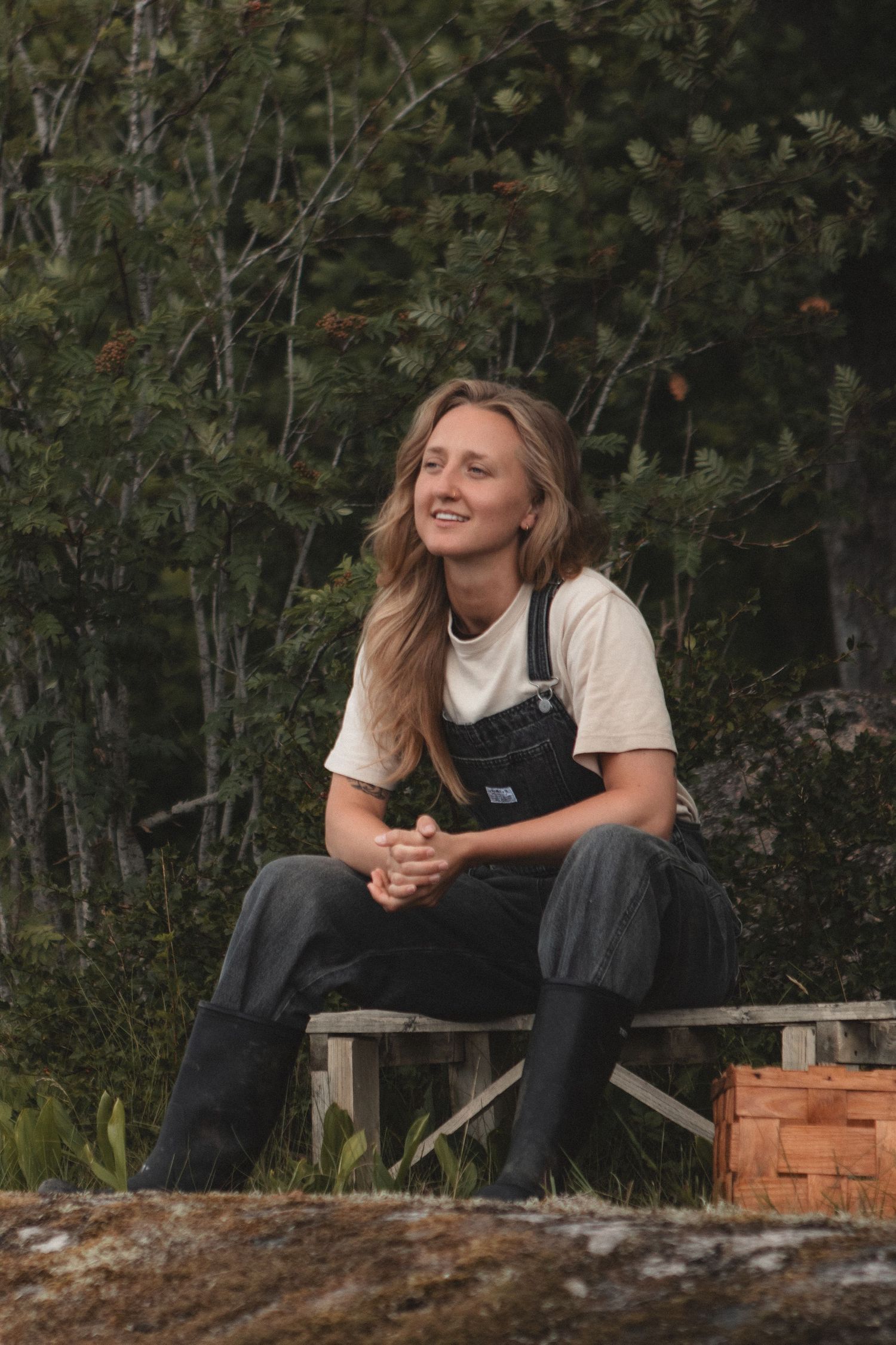 A forager in overalls sits smiling on a wooden bench with harvest crates nearby.