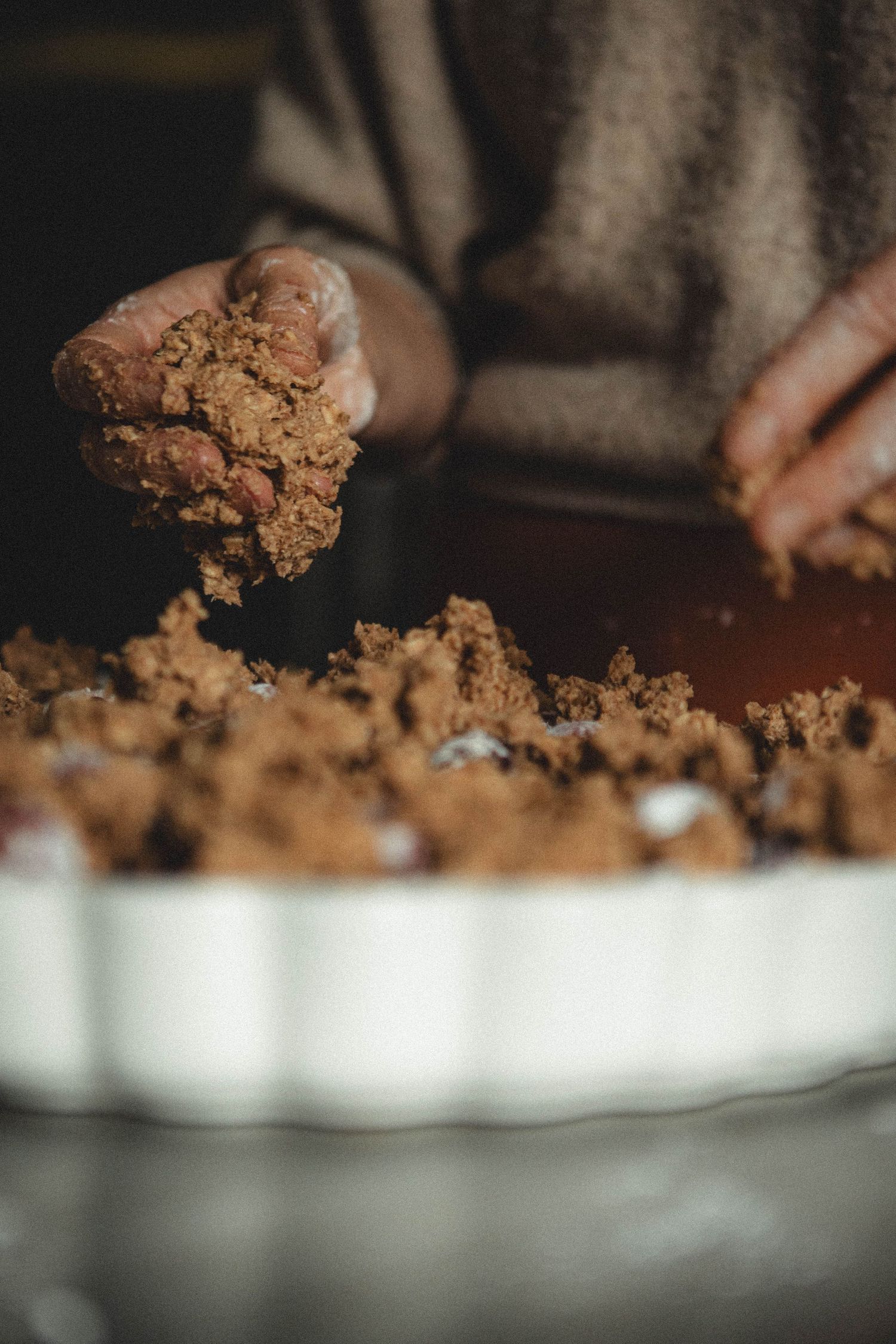 Close-up of hands crumbling chocolate cookie mixture into a white baking dish.