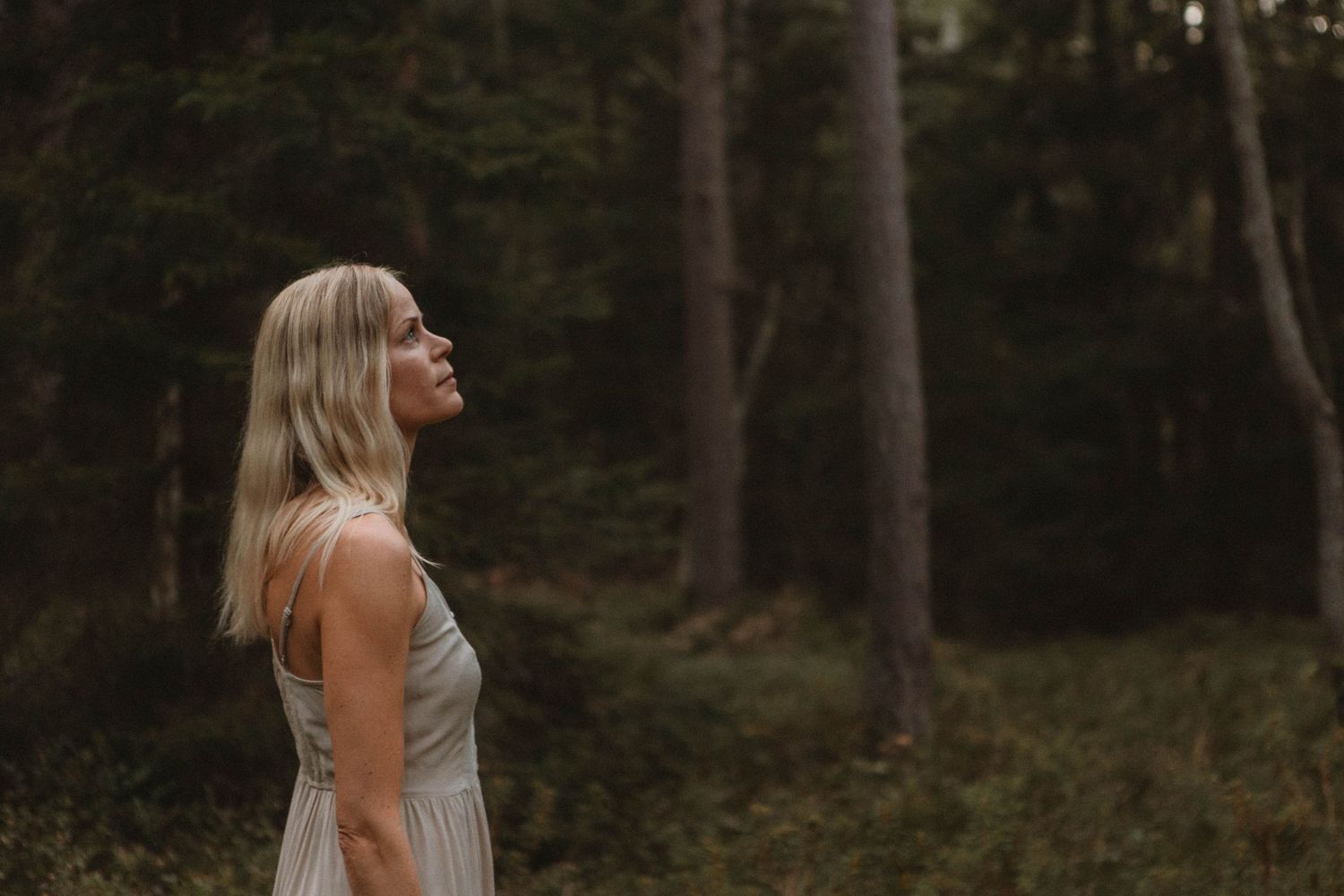 Figure in light dress stands peacefully in sunlit forest clearing.
