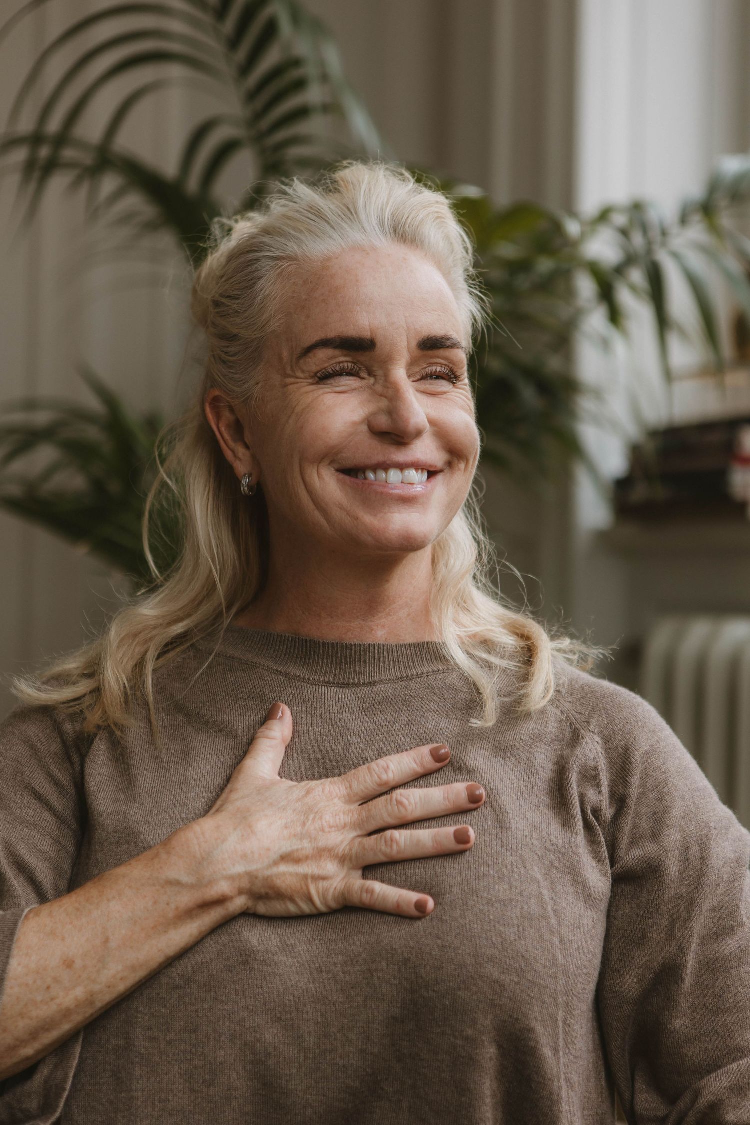 Person in brown sweater smiles warmly while practicing mindfulness exercises at home.
