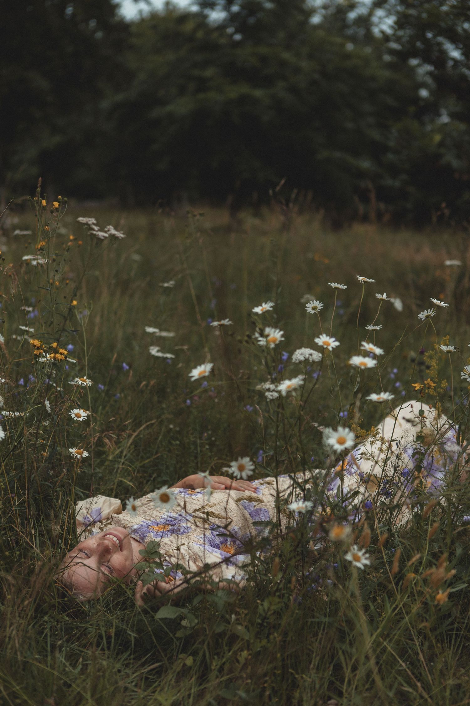 A floral print dress blends into a dreamy meadow of wild daisies and tall grass at dusk.