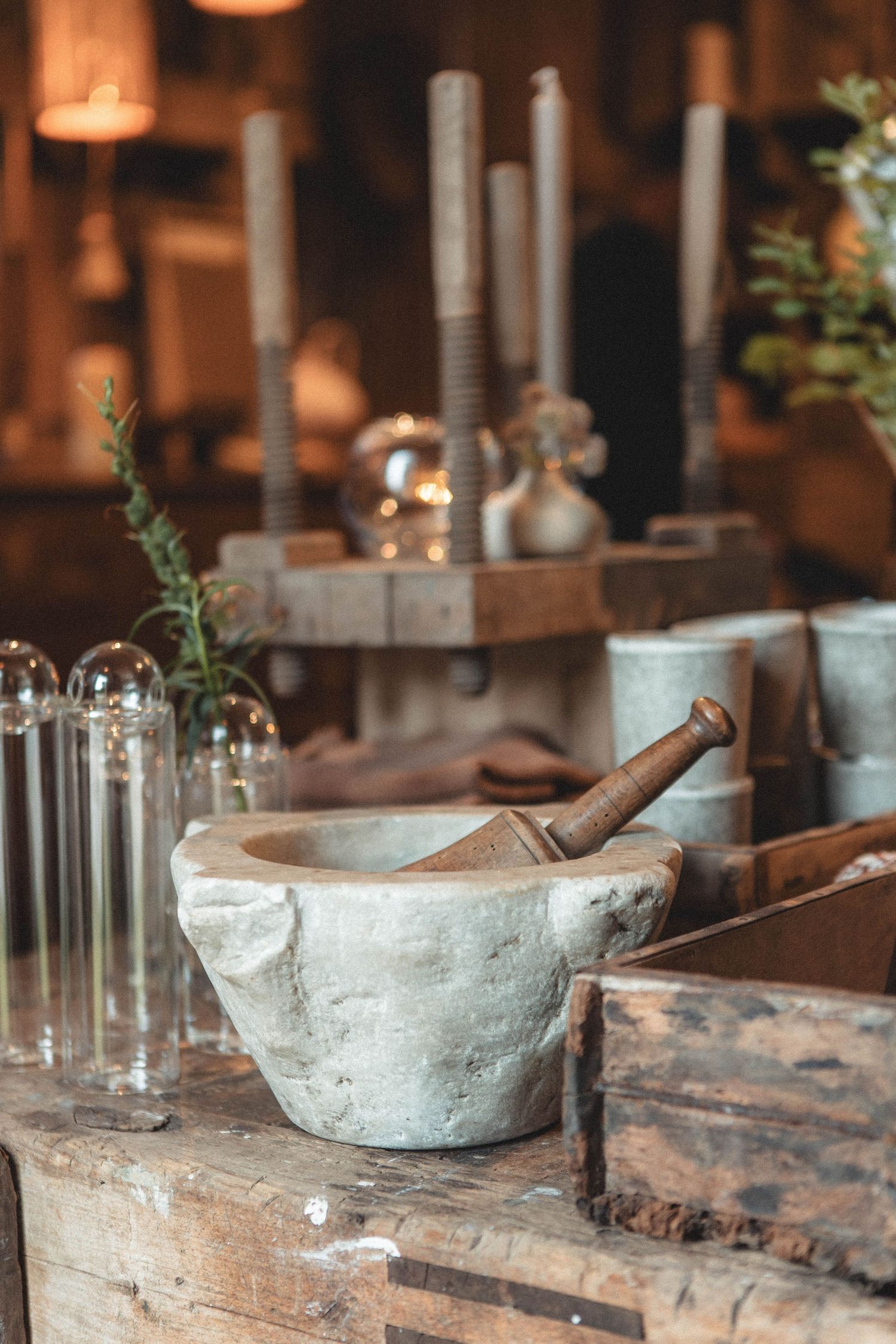 Vintage-style still life with mortar and pestle, candles, and glass vessels on wooden surface.