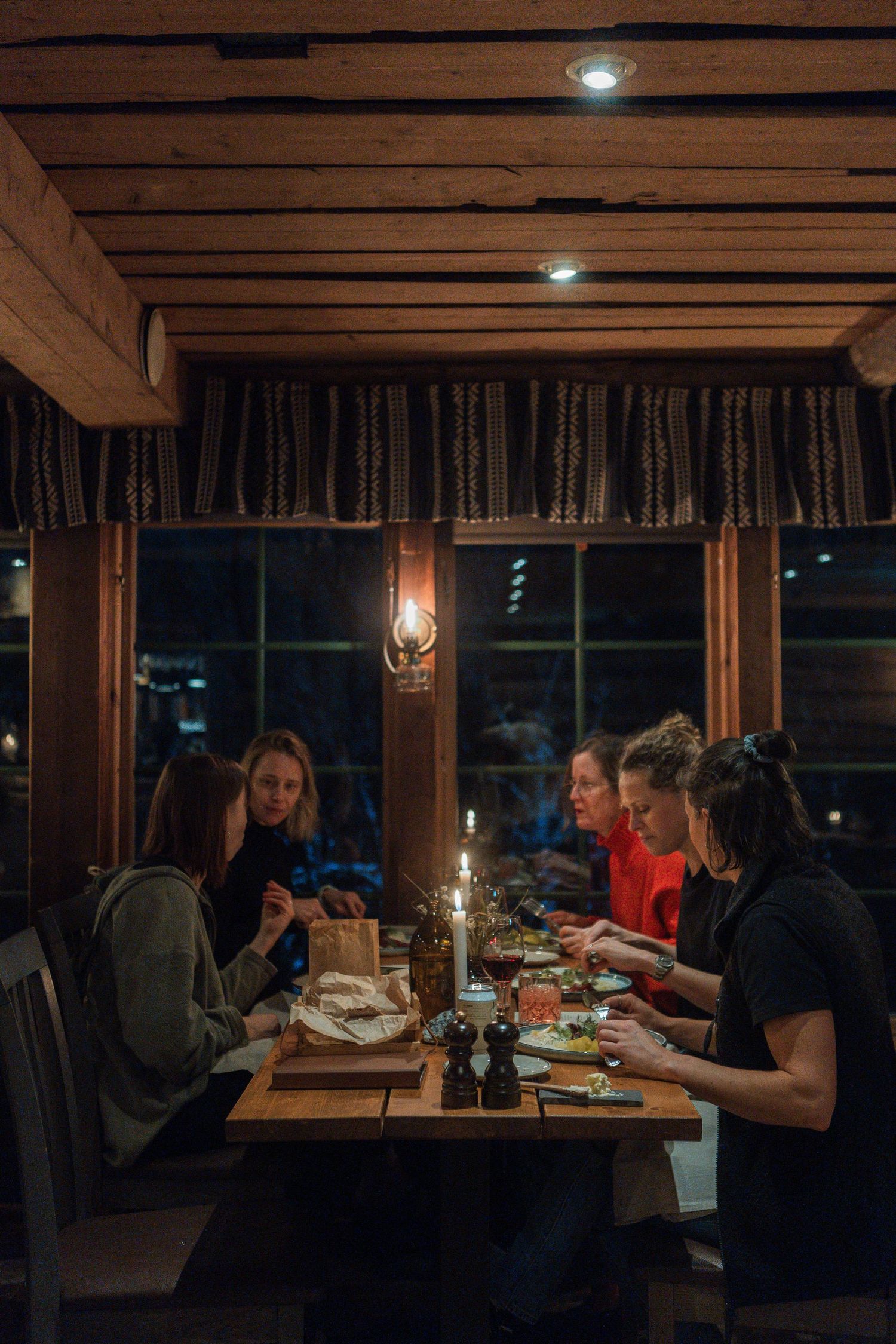 Group dining at rustic wooden table by candlelight under timber ceiling.