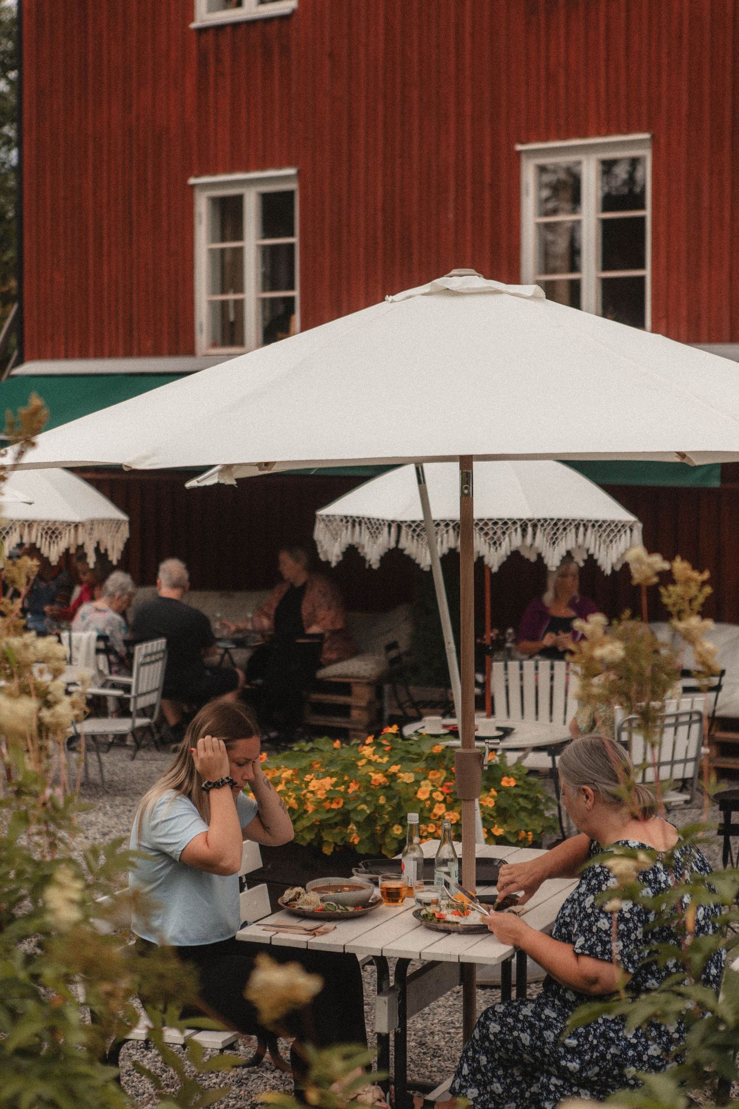 Garden cafe setting with white umbrellas and diners enjoying meals outdoors.