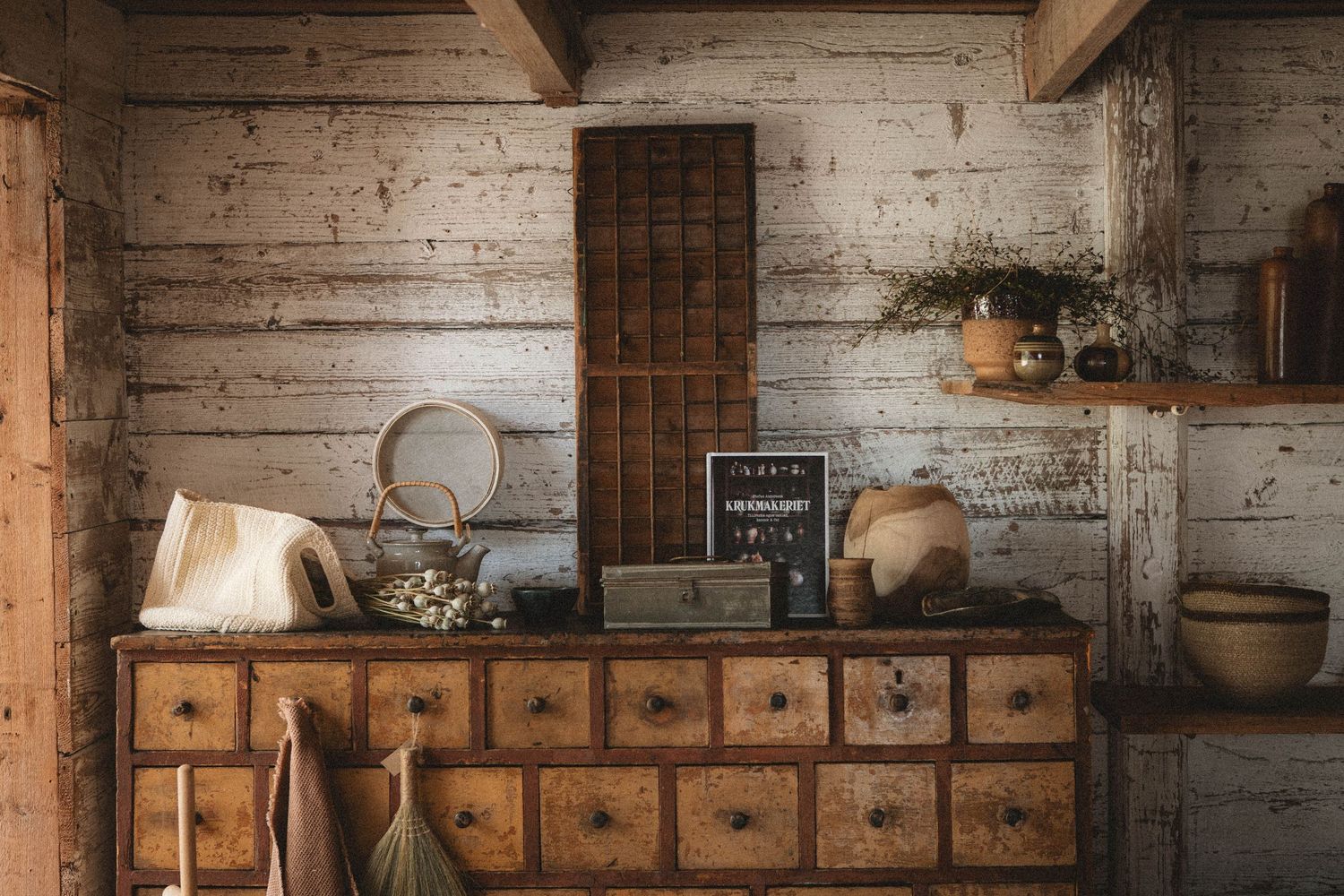 Vintage apothecary cabinet with wooden drawers against white-washed wall in rustic kitchen.