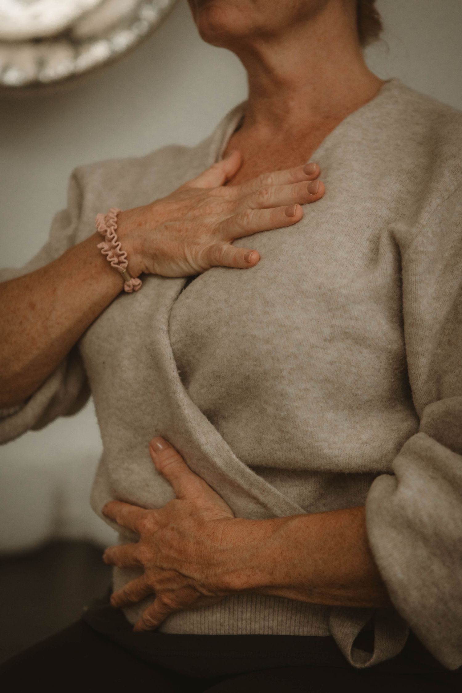 A person wearing a beige sweater with delicate hands crossed over their chest and a rose gold bracelet.