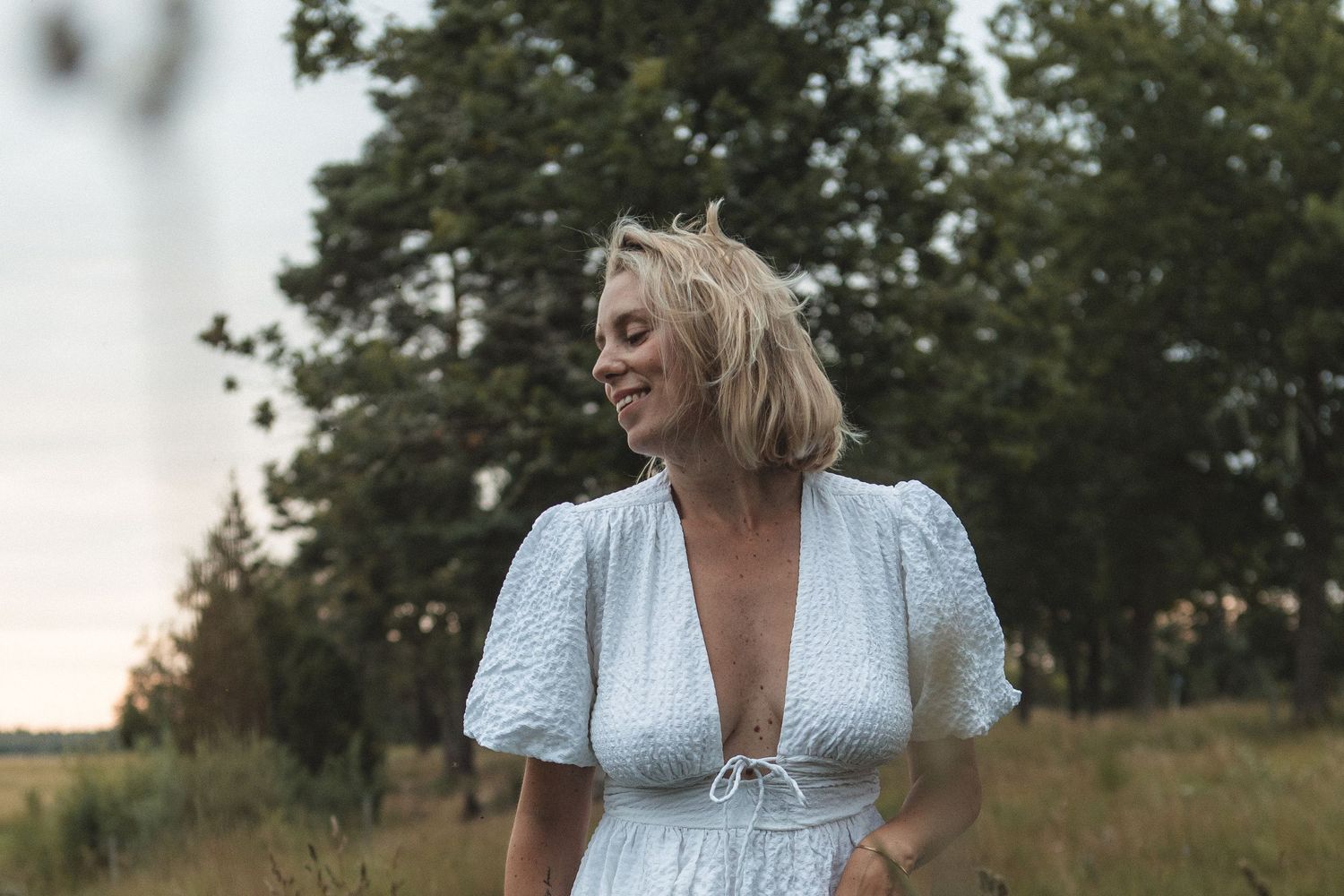 Someone wearing a white dress laughs joyfully in a field during golden hour.