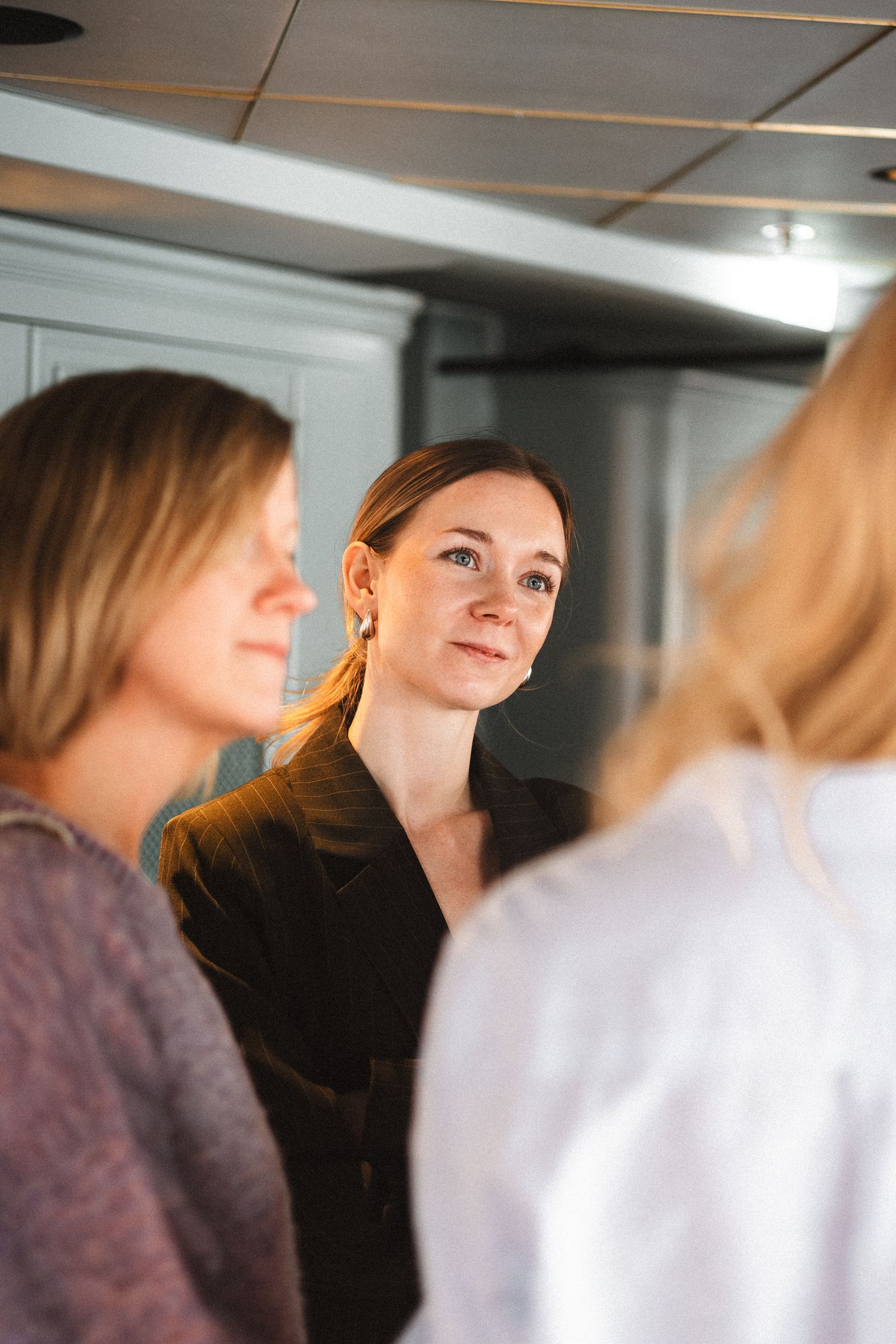 A small group engages in conversation in an office or meeting space with natural lighting.