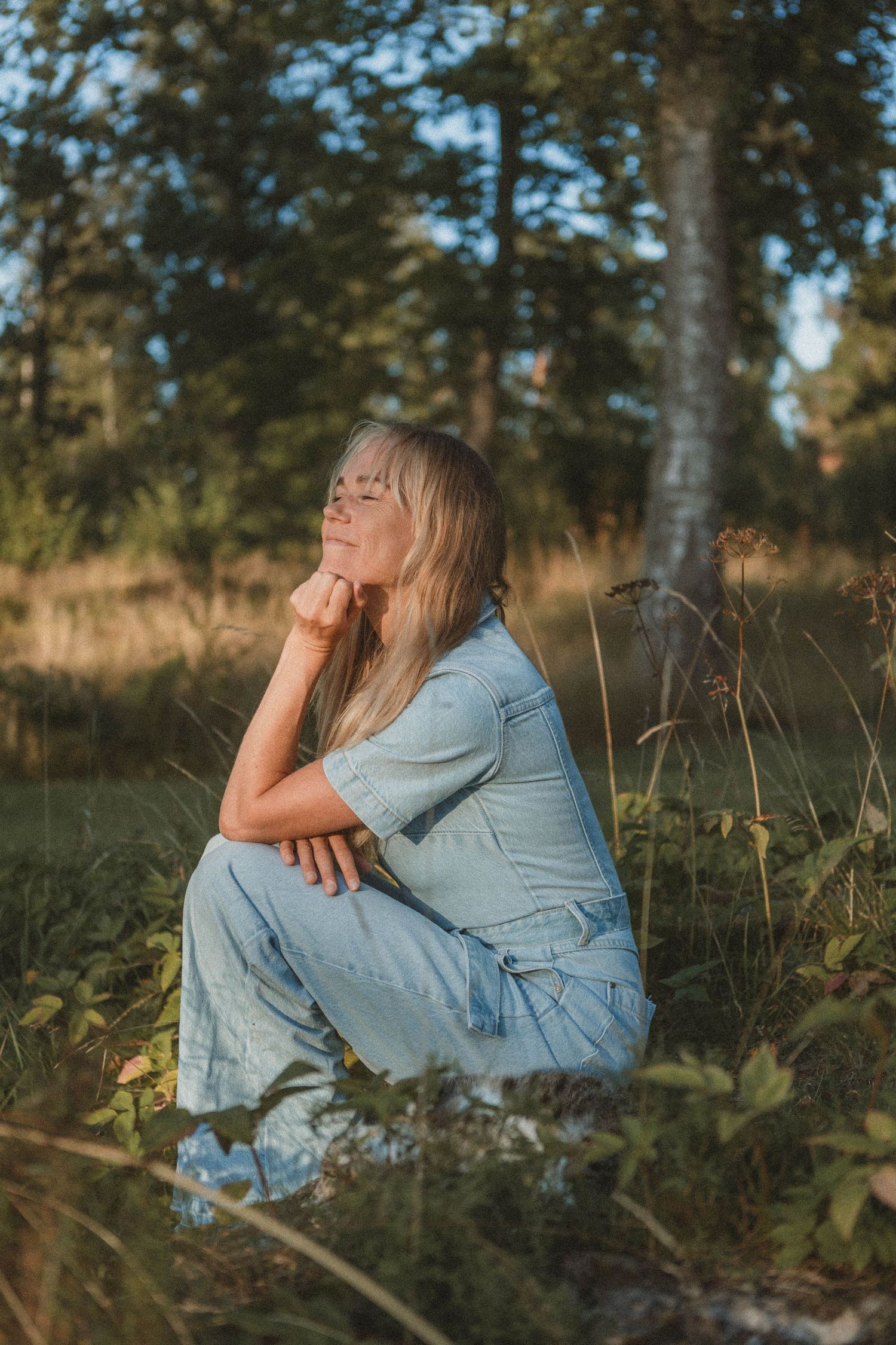 Contemplative figure in denim sitting among trees during golden hour.