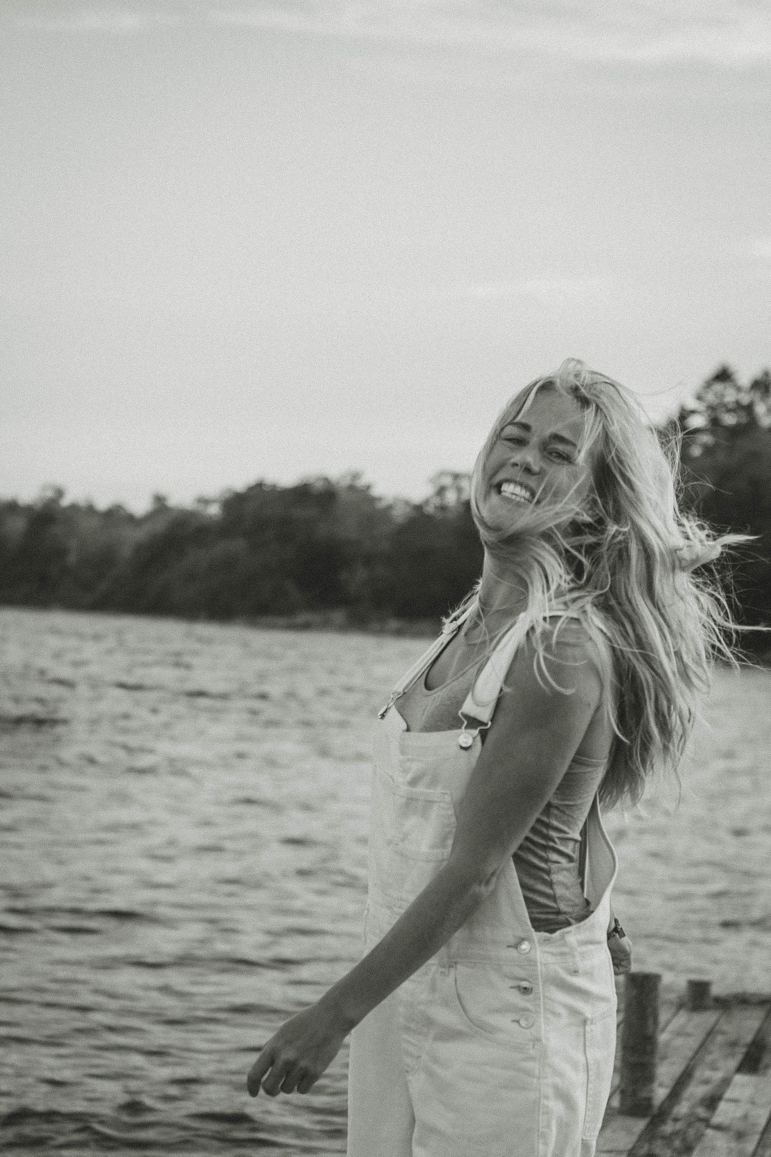 Black and white portrait of someone laughing in overalls on wooden dock.