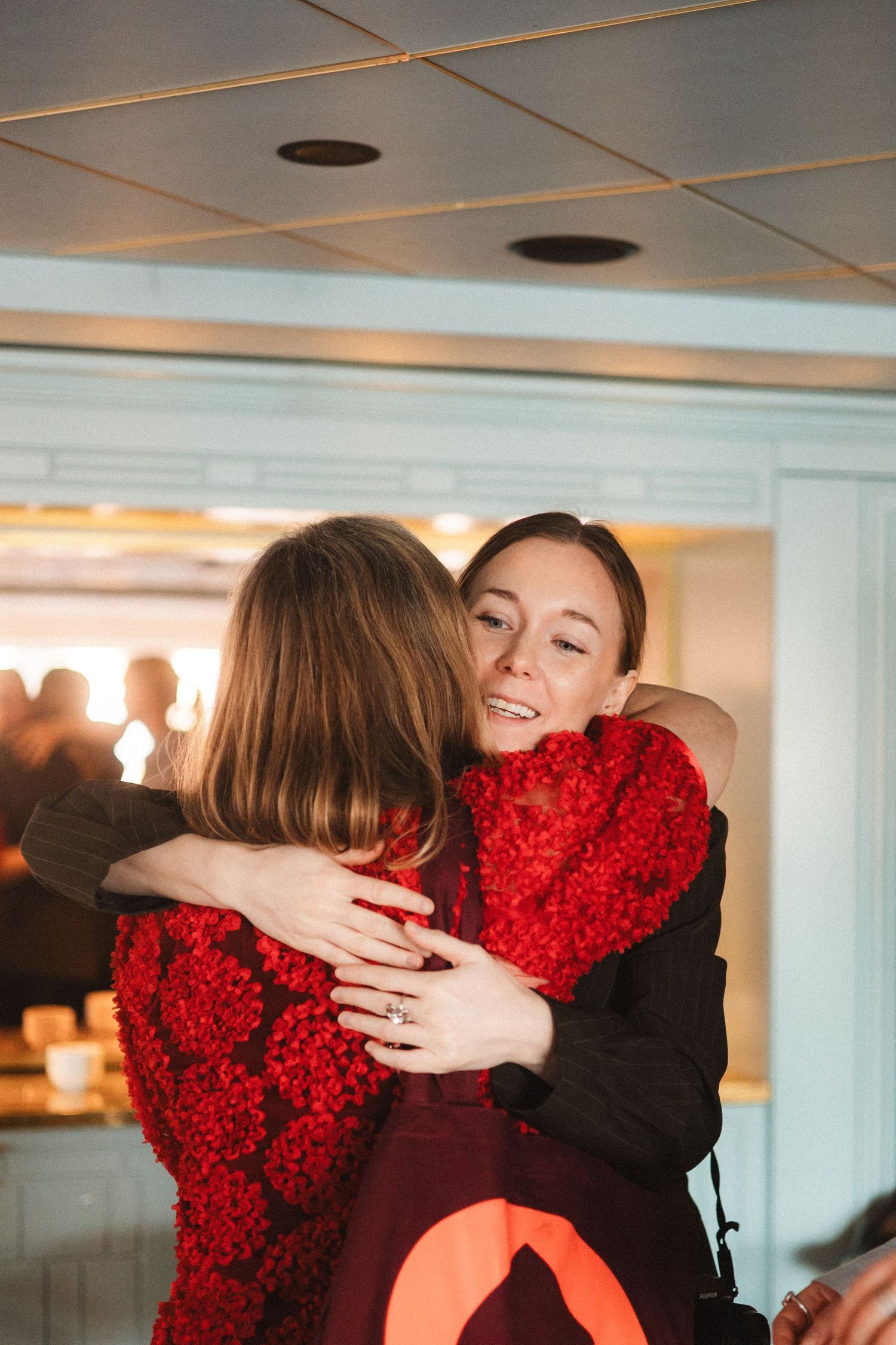 Two people embrace warmly while one holds a large bouquet of bright red flowers.