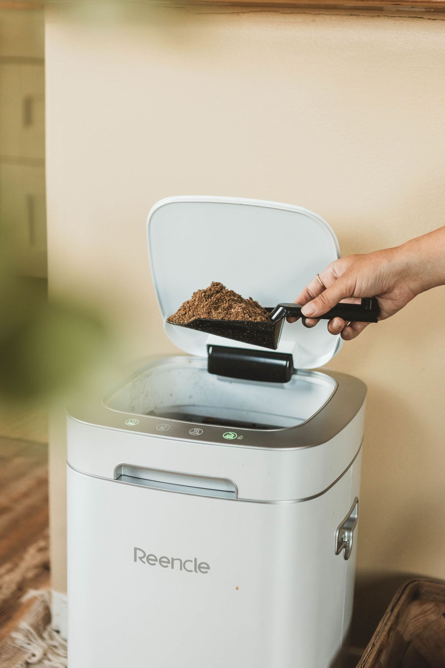 Hand adding food waste into a sleek white countertop composting machine.