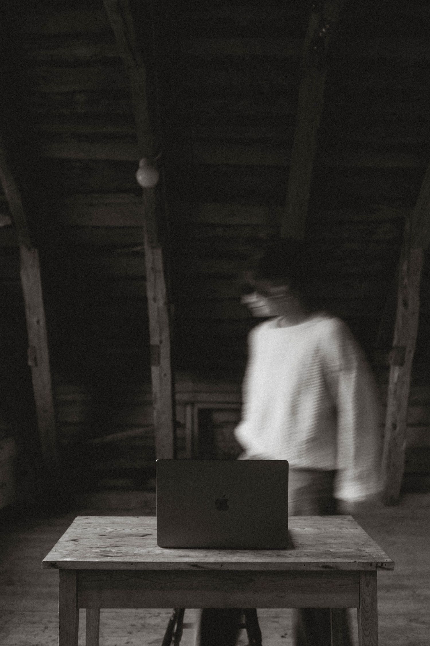 Artistic motion blur photo of laptop on wooden table in dark attic space.