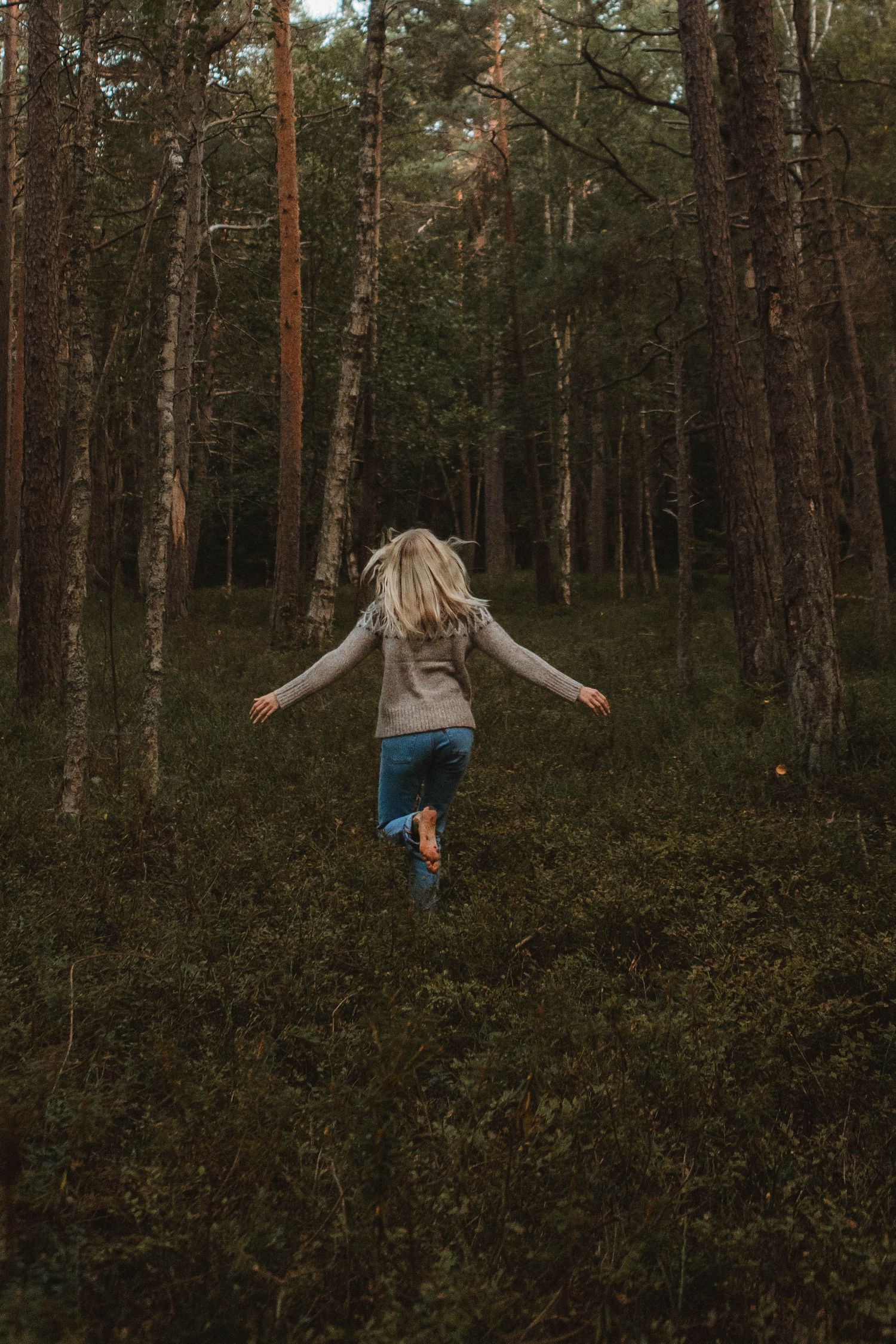 Someone in a casual sweater runs joyfully through a dense pine forest.