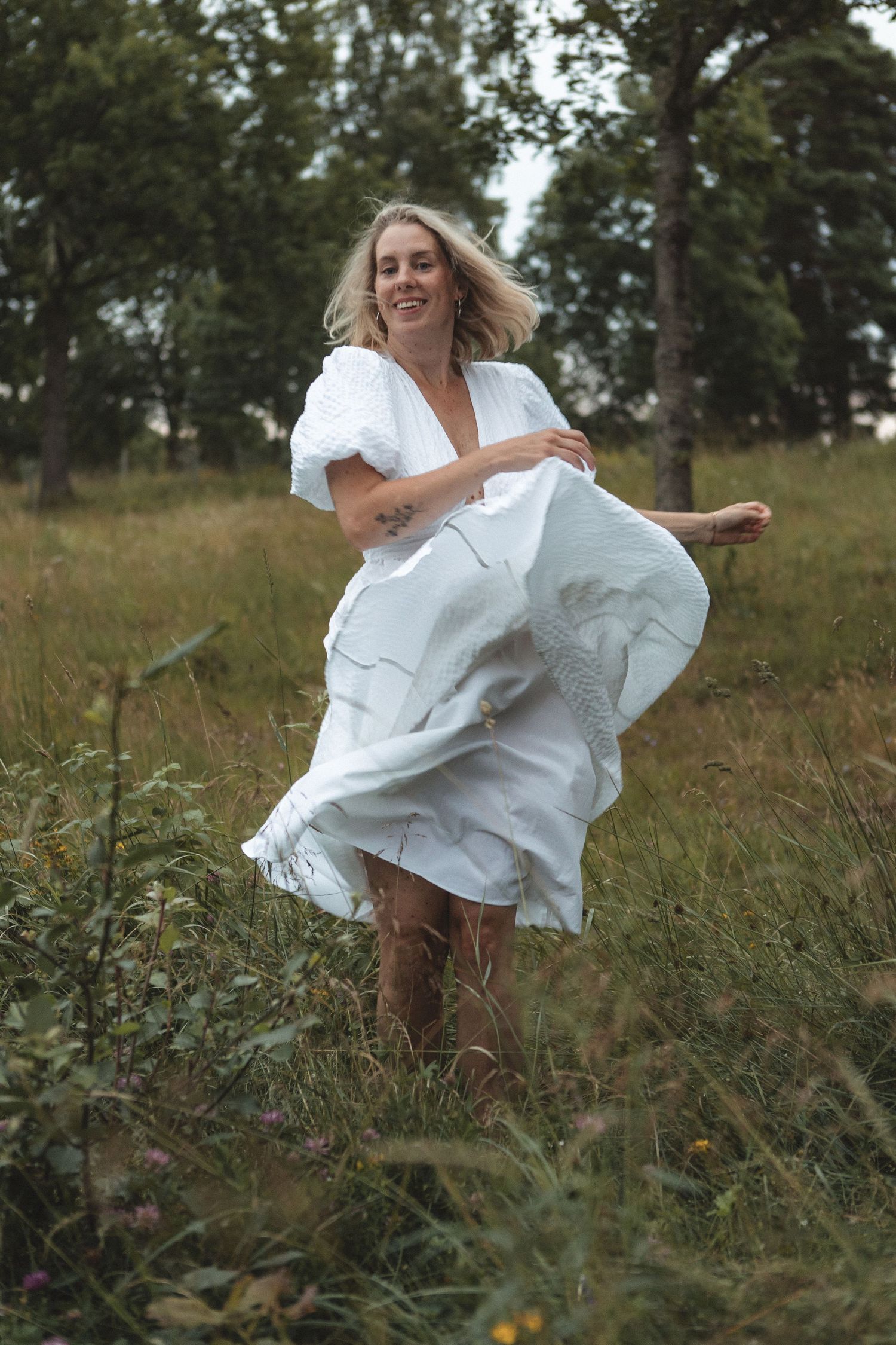 White dress billowing in the wind as someone dances through a rural field.