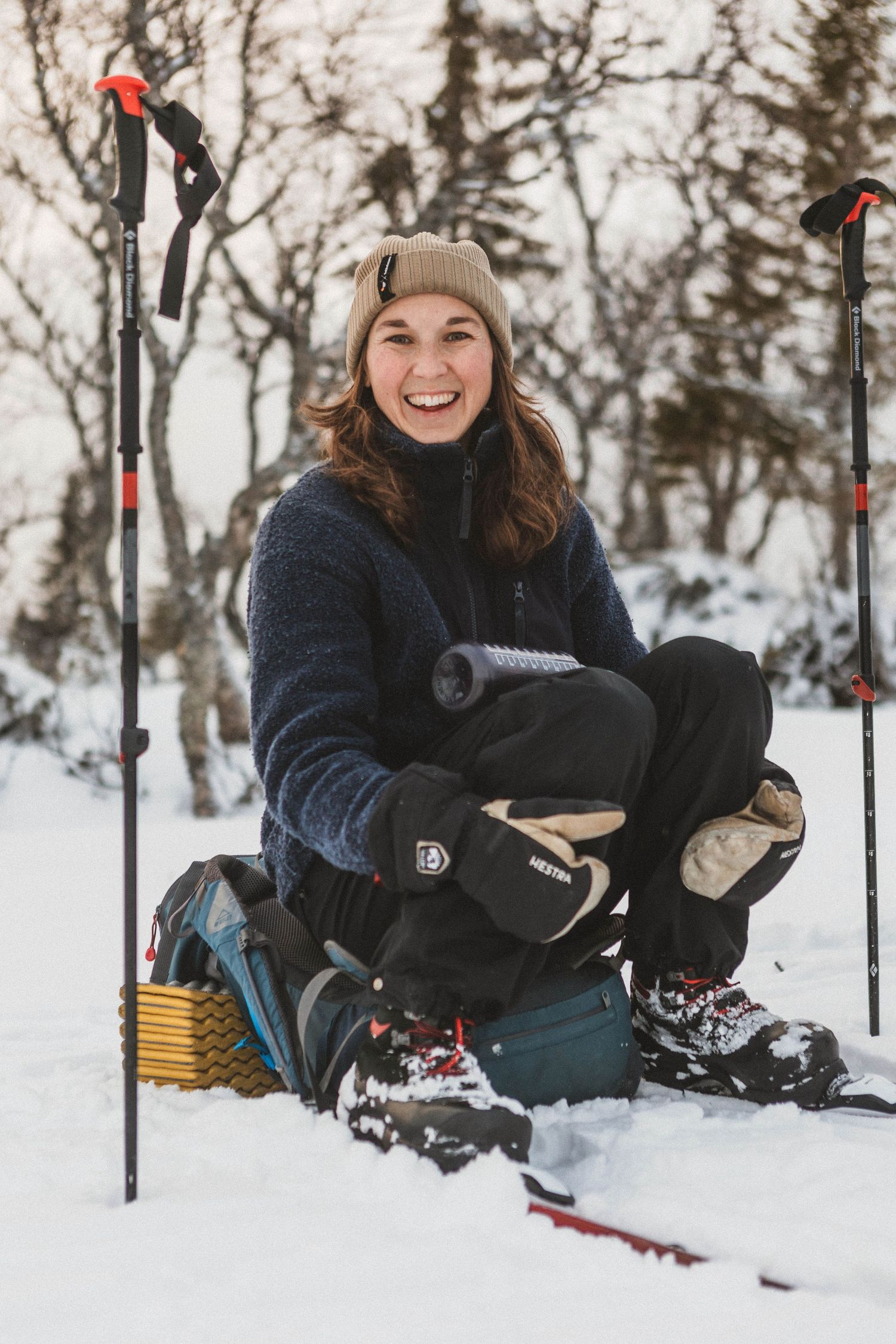 Winter sports enthusiast takes a break in the snow with skiing poles and warm winter gear on snowy terrain.
