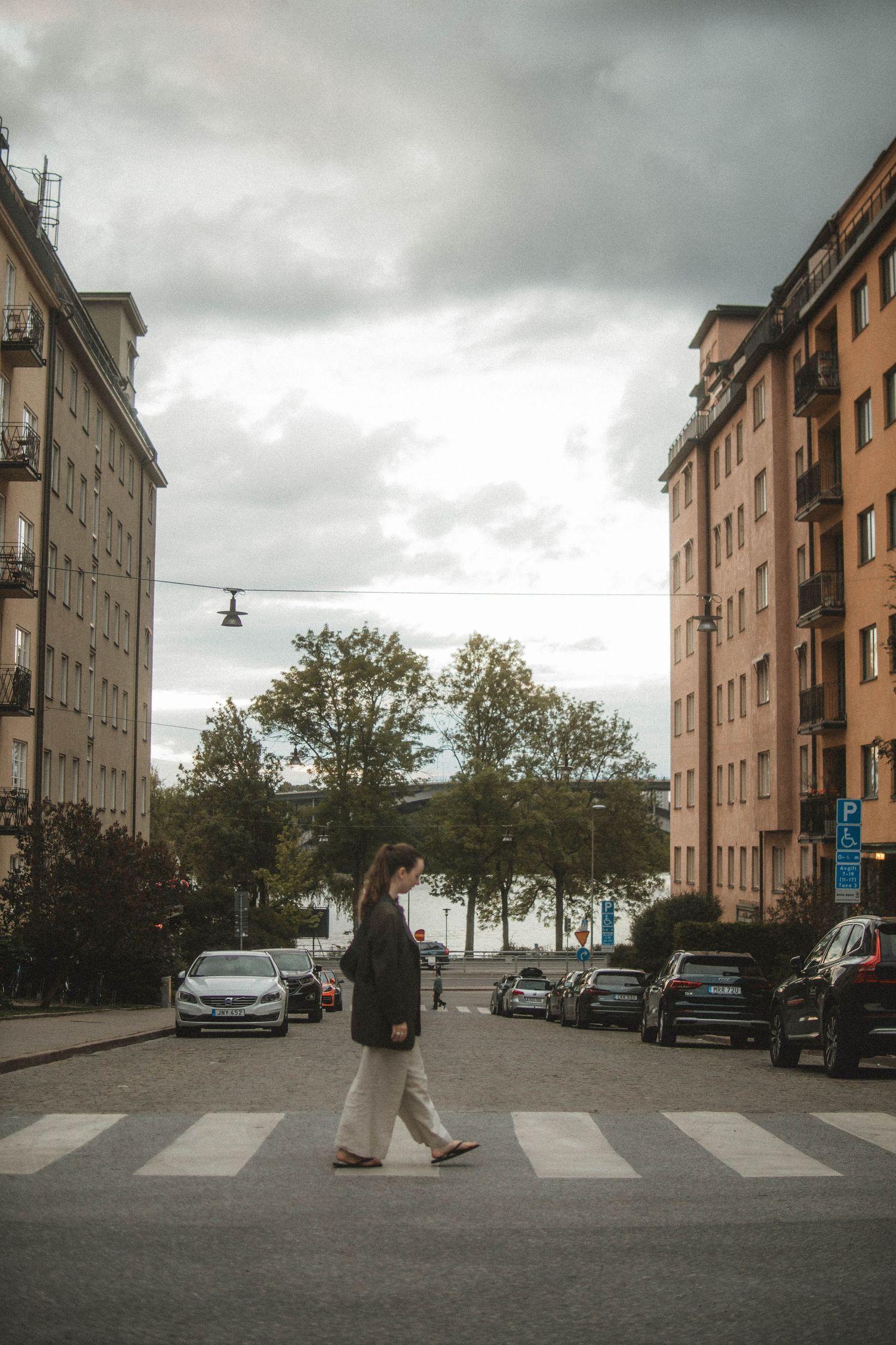 A person crosses a zebra crossing between apartment buildings on a cloudy day in an urban neighborhood.