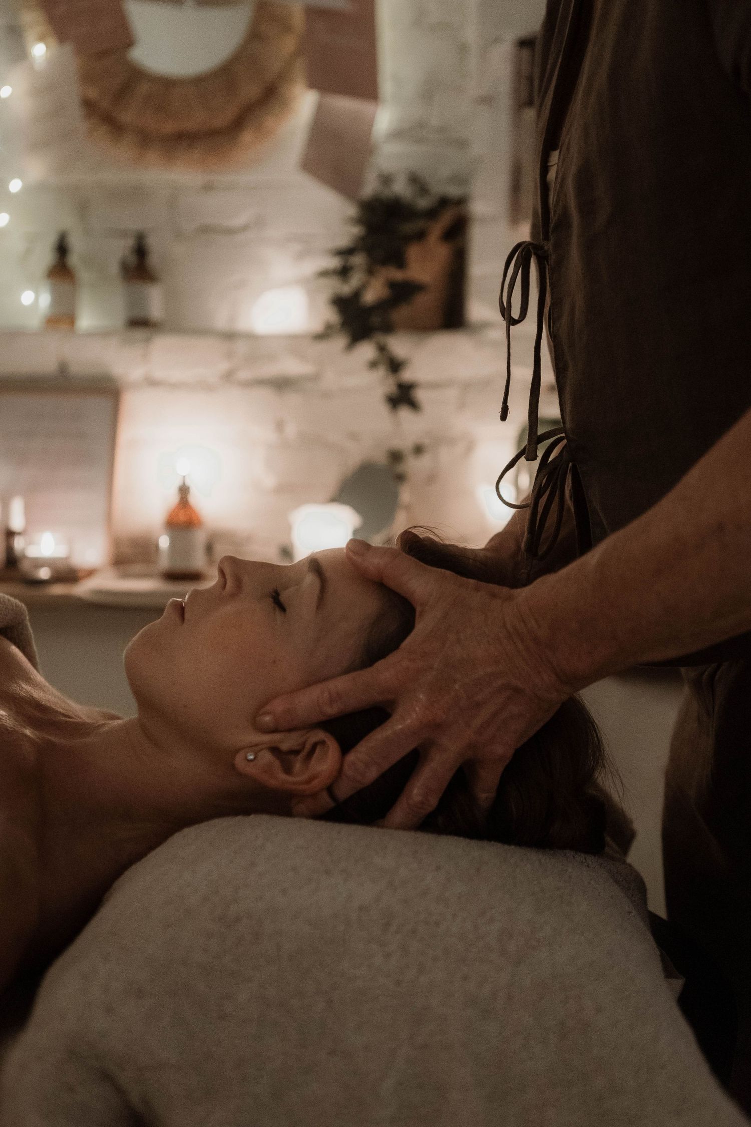 Therapeutic head massage being performed in a candlelit spa room with decorative elements.