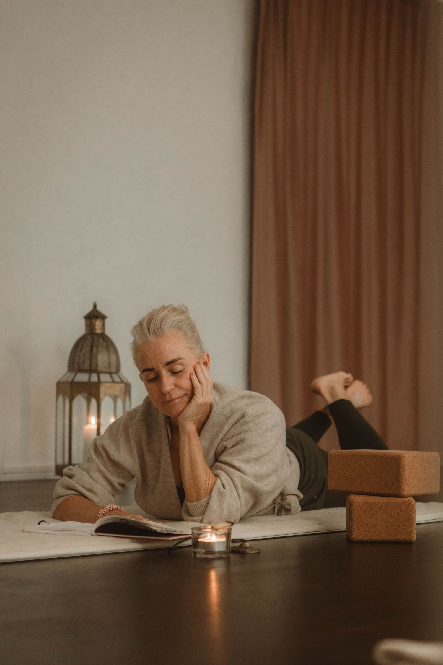 Person relaxing with a book at a wooden table with lantern and candle creating cozy atmosphere in warm lighting.