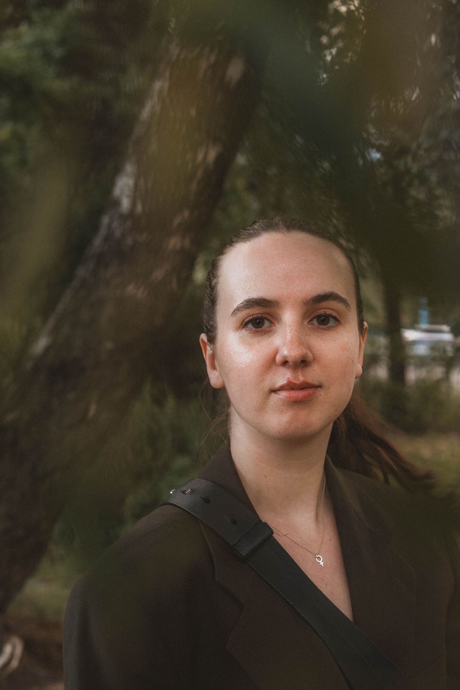 Portrait of someone in a dark jacket against a blurred forest background with soft natural lighting.