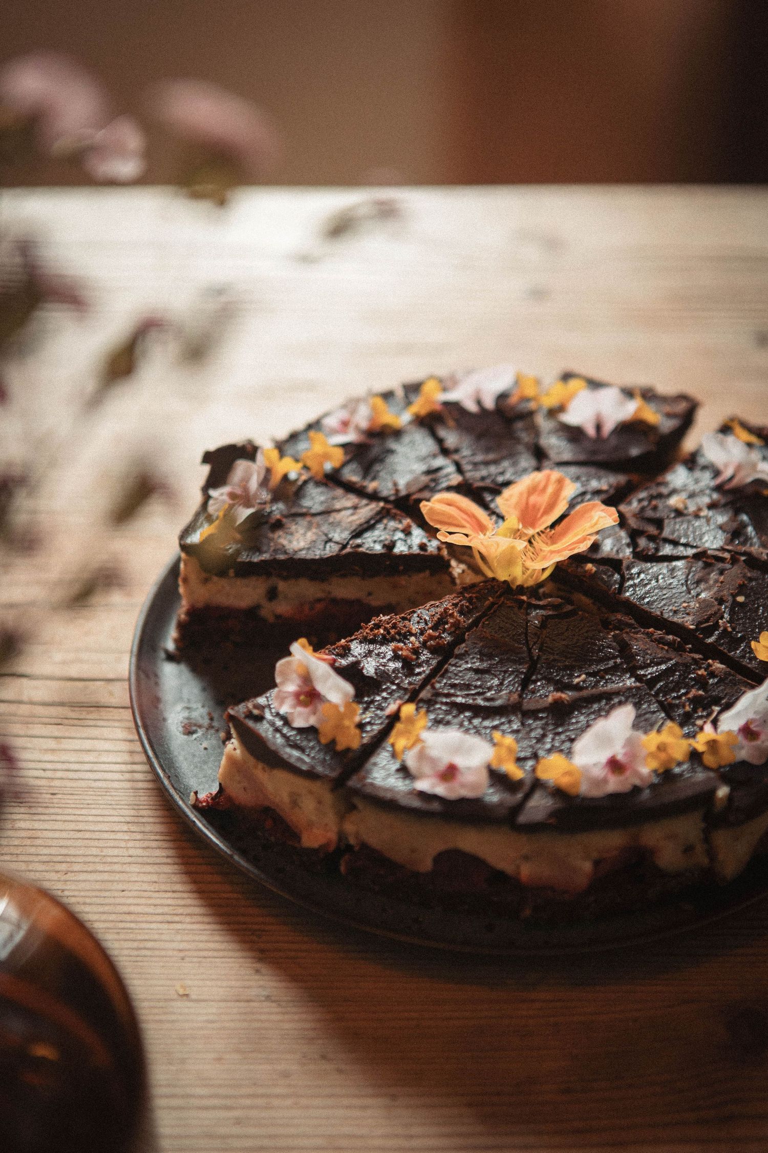 Chocolate cake decorated with edible flowers and geometric patterns served on dark plate.