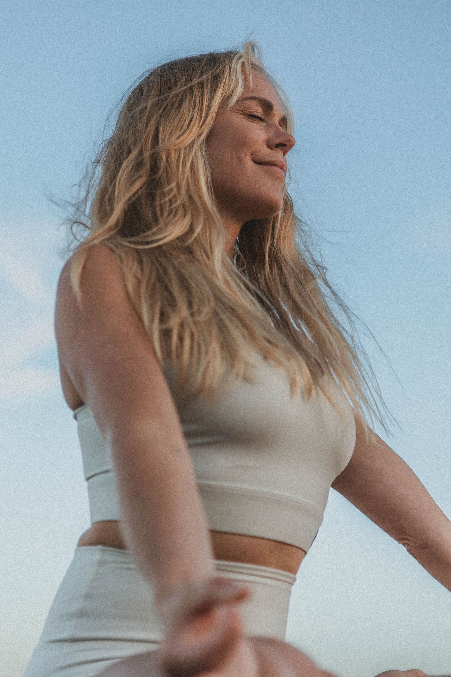 Carefree moment in white crop top against blue sky with wind-swept hair.