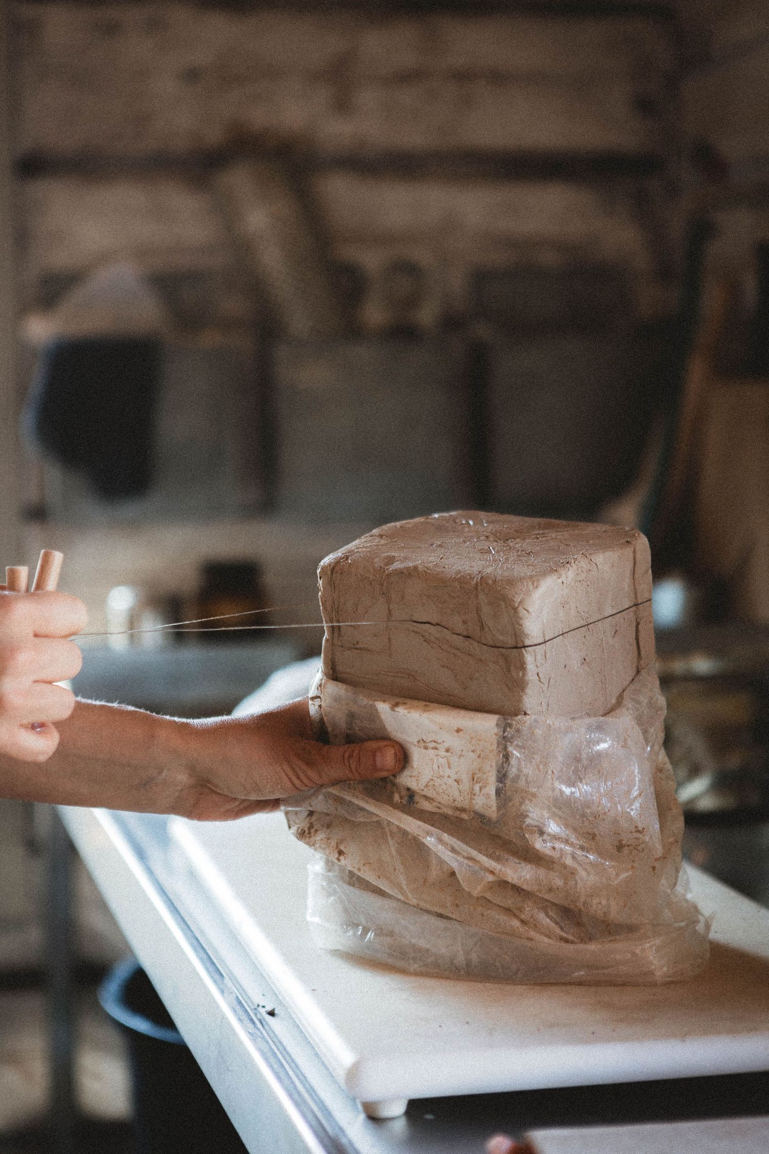 Hands shaping clay or dough on white surface in rustic kitchen setting.