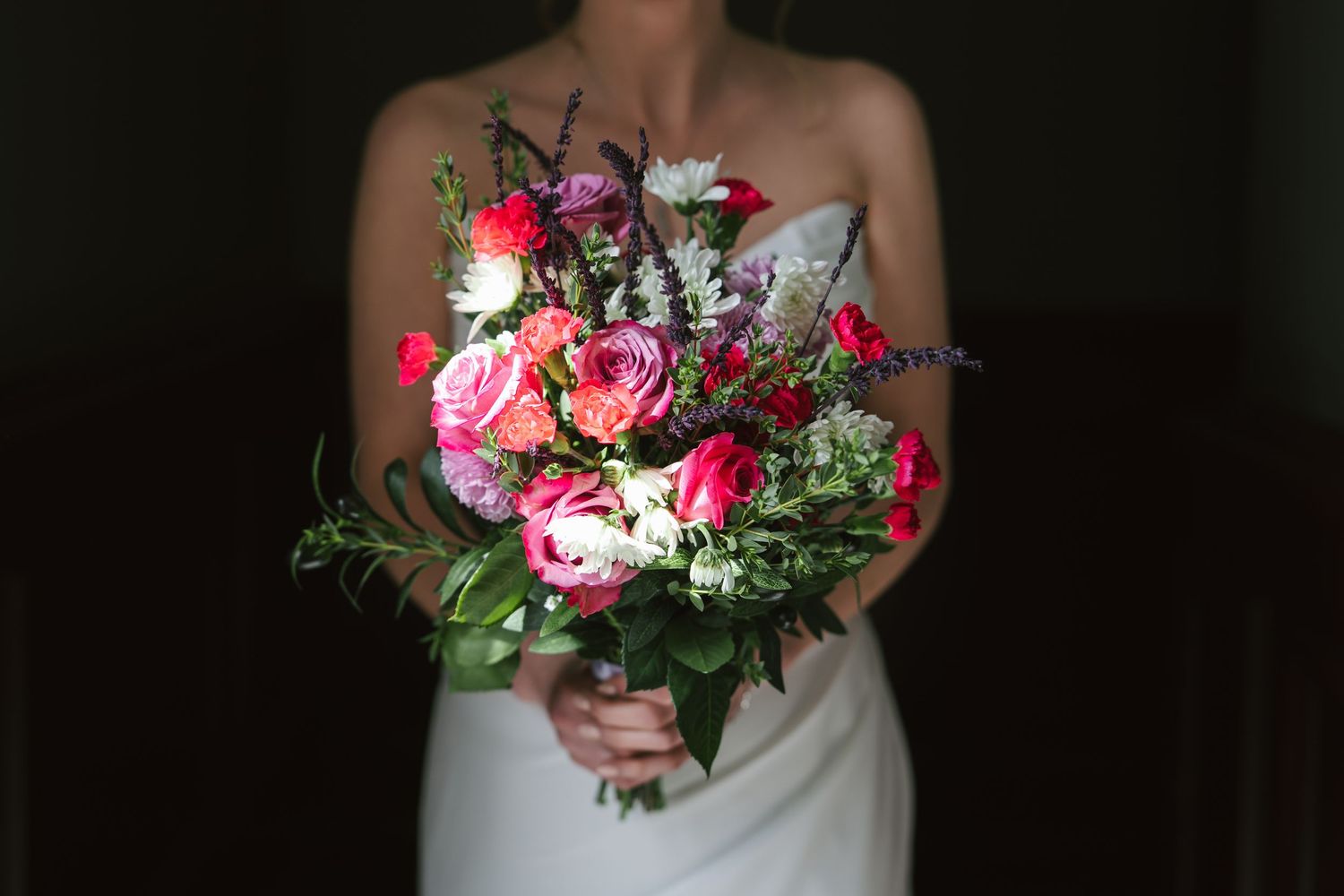 A colorful wedding bouquet featuring pink and white flowers with greenery against a dark background.