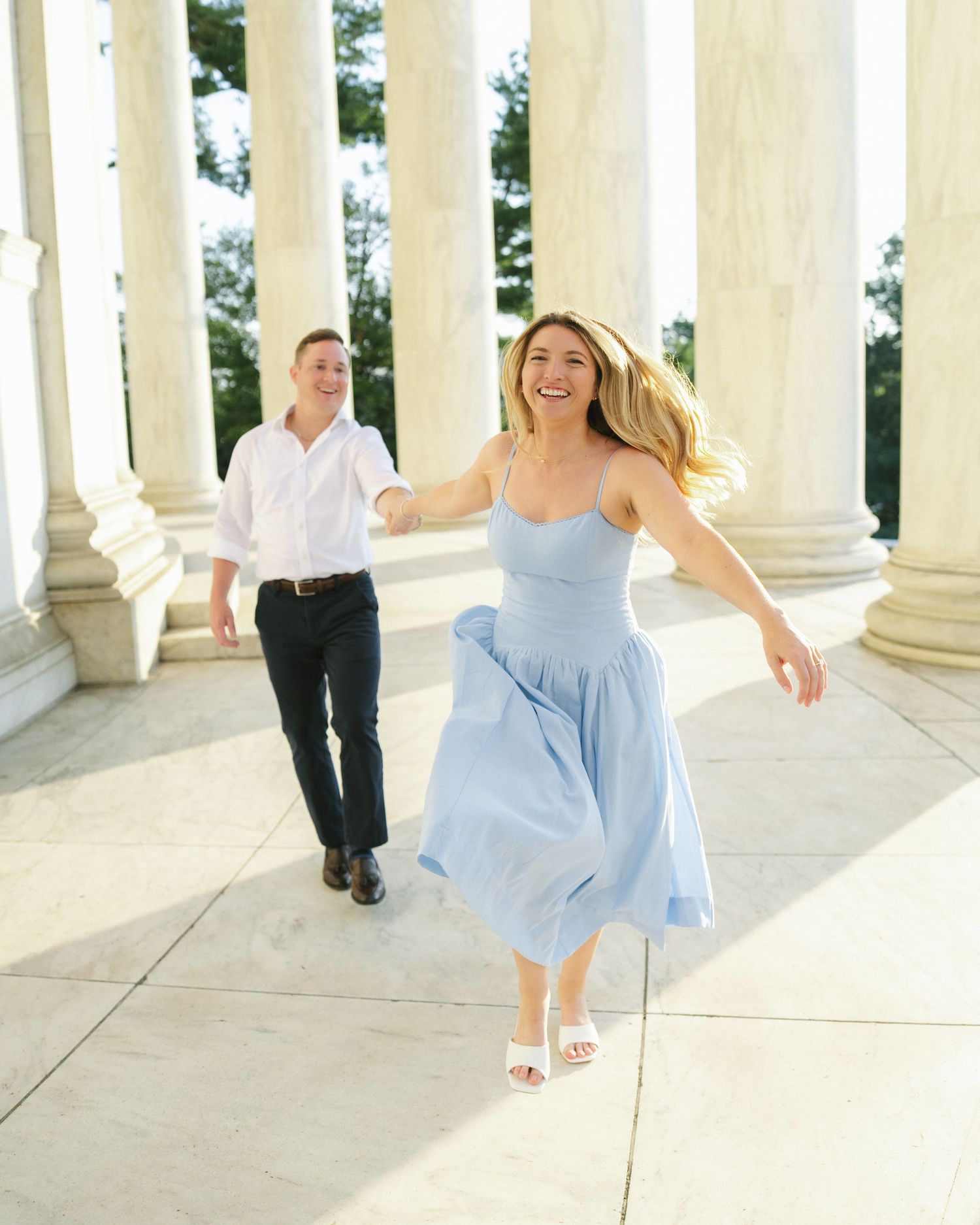 A young couple walking together on a sunny day, with the woman in a light blue dress and the man in a white shirt.