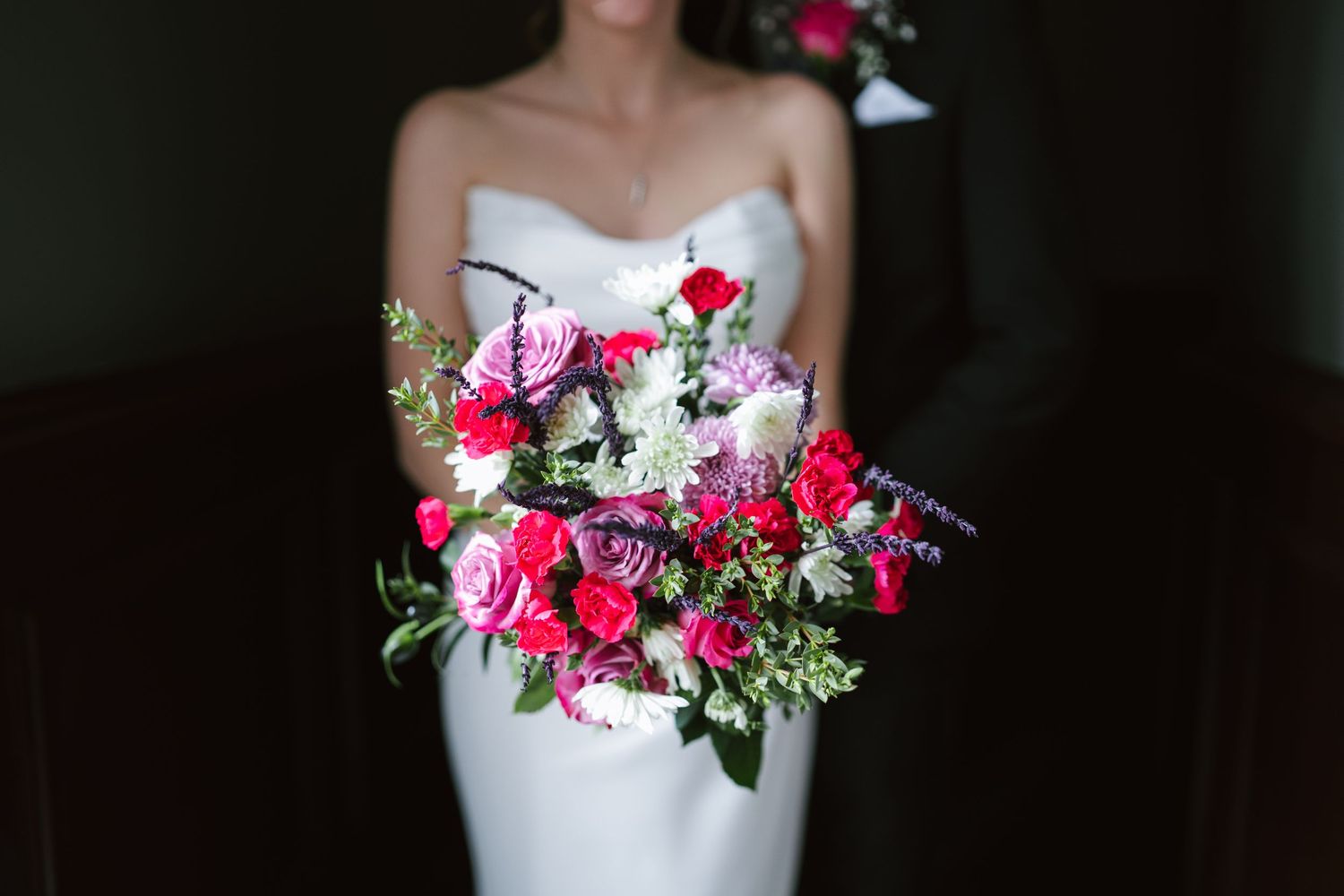 A wedding bouquet with vibrant pink and white flowers arranged with greenery against a white dress.
