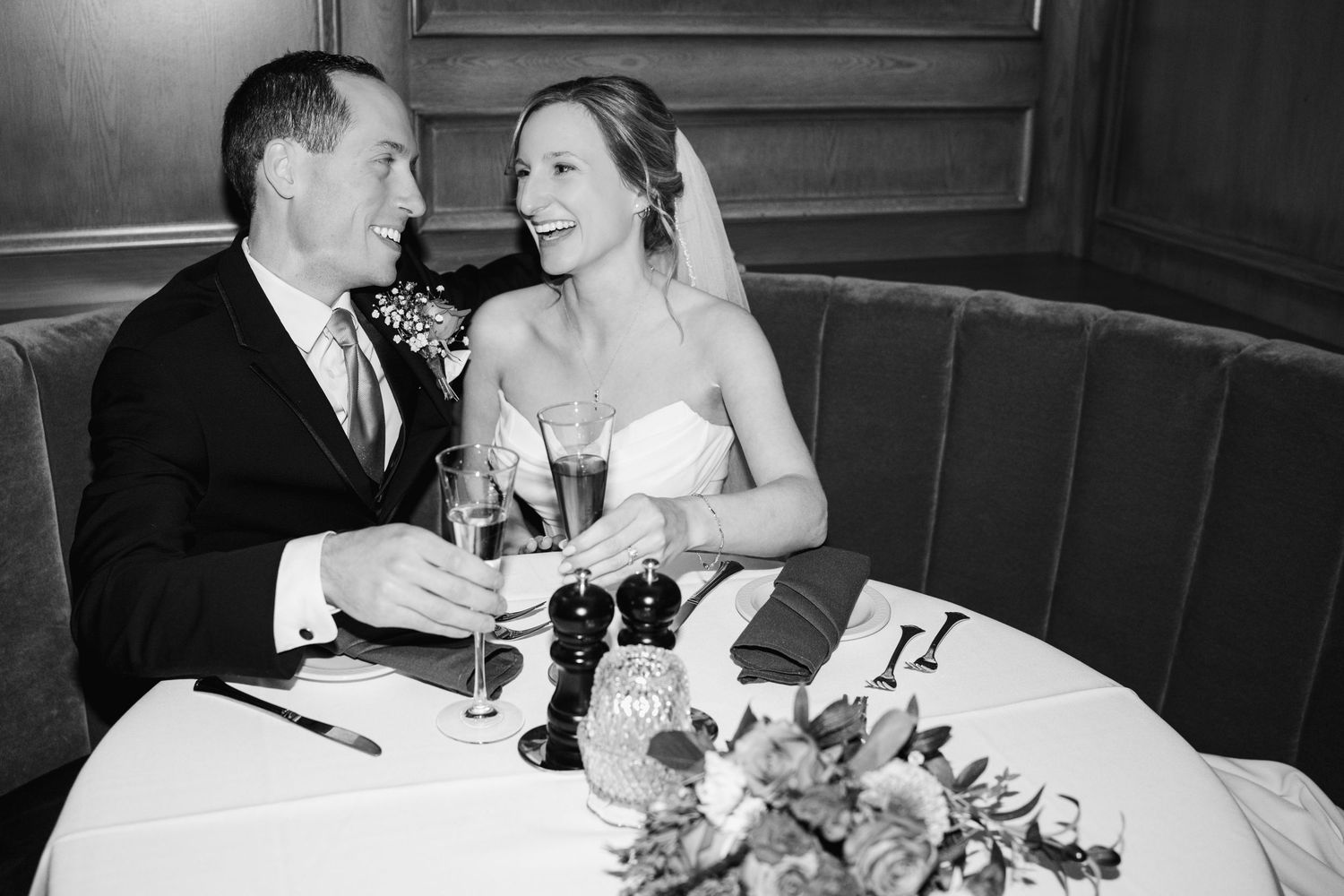 A bride and groom share an intimate moment at their wedding reception while seated in a curved booth with champagne.
