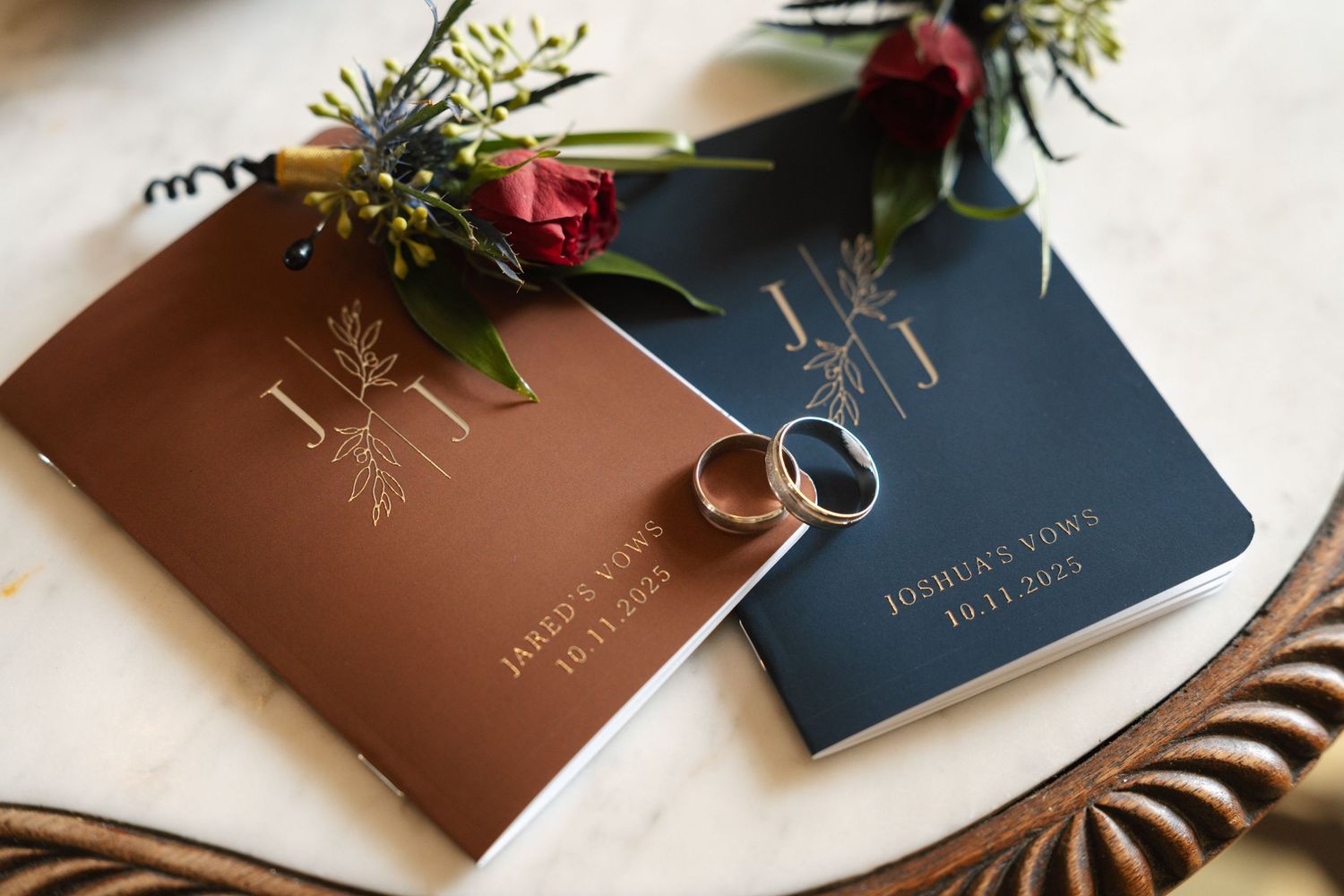 An image of a pair of wedding rings on a brown leather book with a floral arrangement.