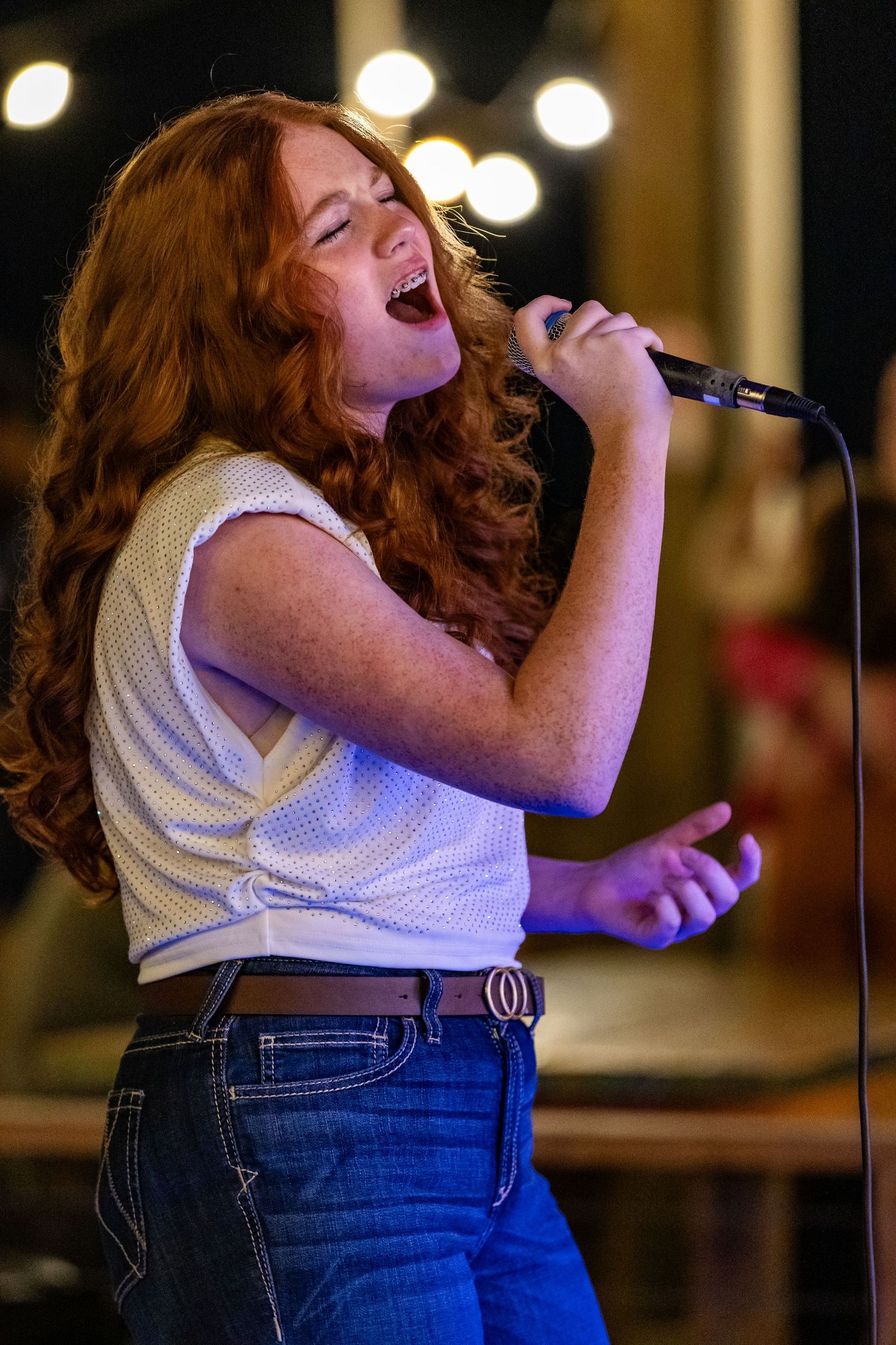 A performer with red hair wearing jeans and a white top sings passionately on stage in a sequence of action shots.