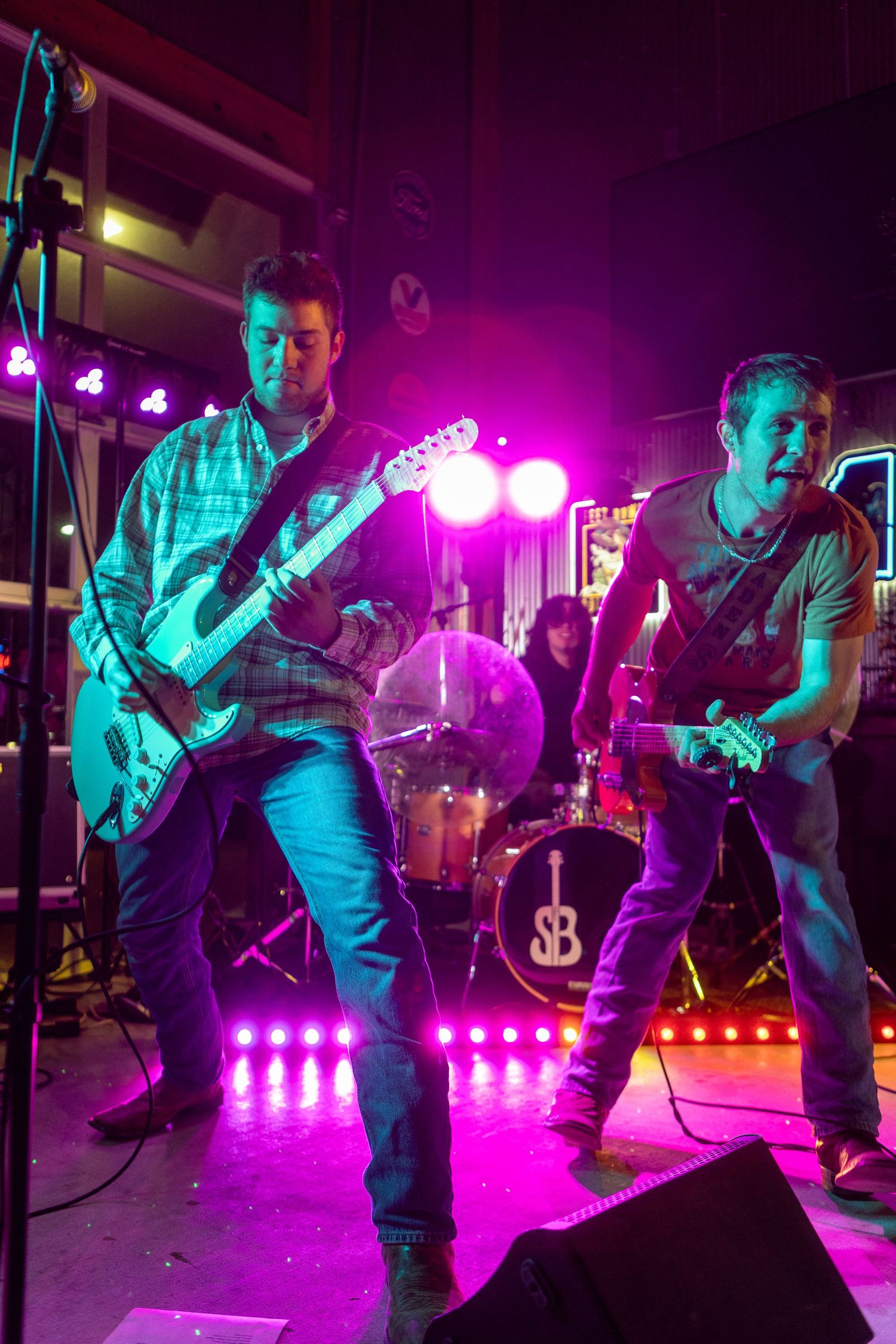 Rock band performs on stage with dramatic pink and teal lighting during an energetic live performance.