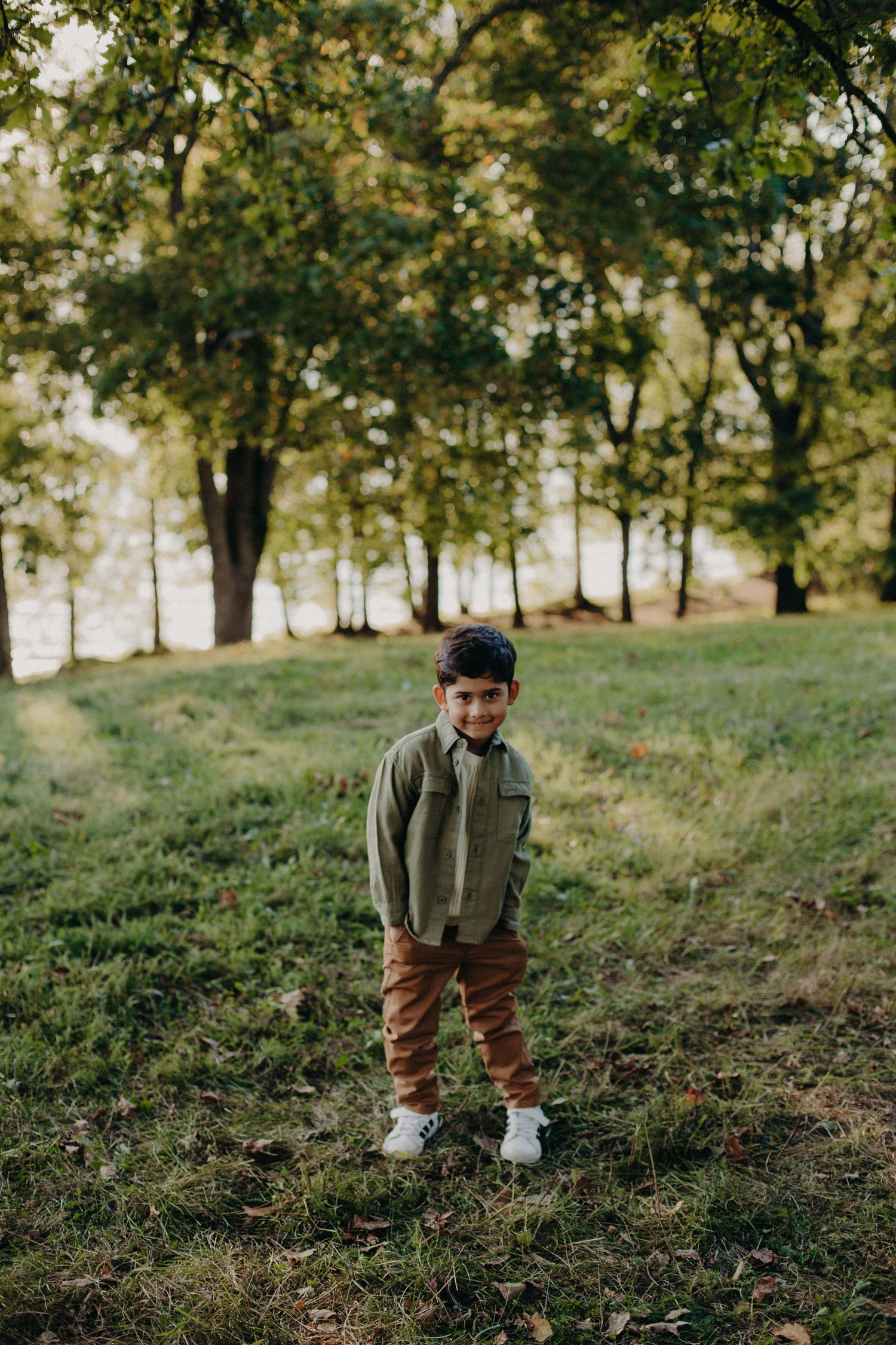 Outdoor lifestyle portrait on grassy hillside with trees in warm evening light.