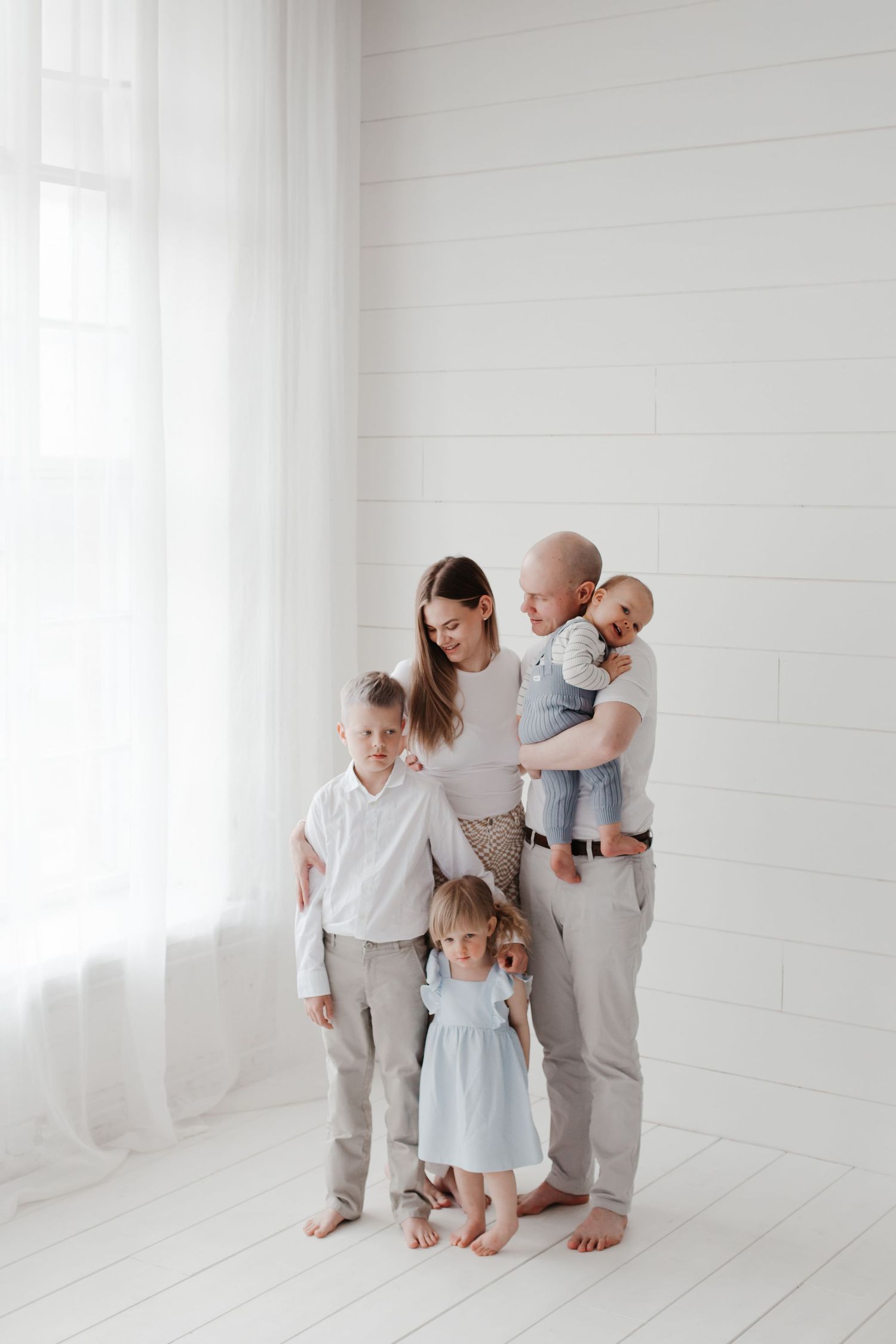 Family group in light colored clothing posing in bright white studio setting.