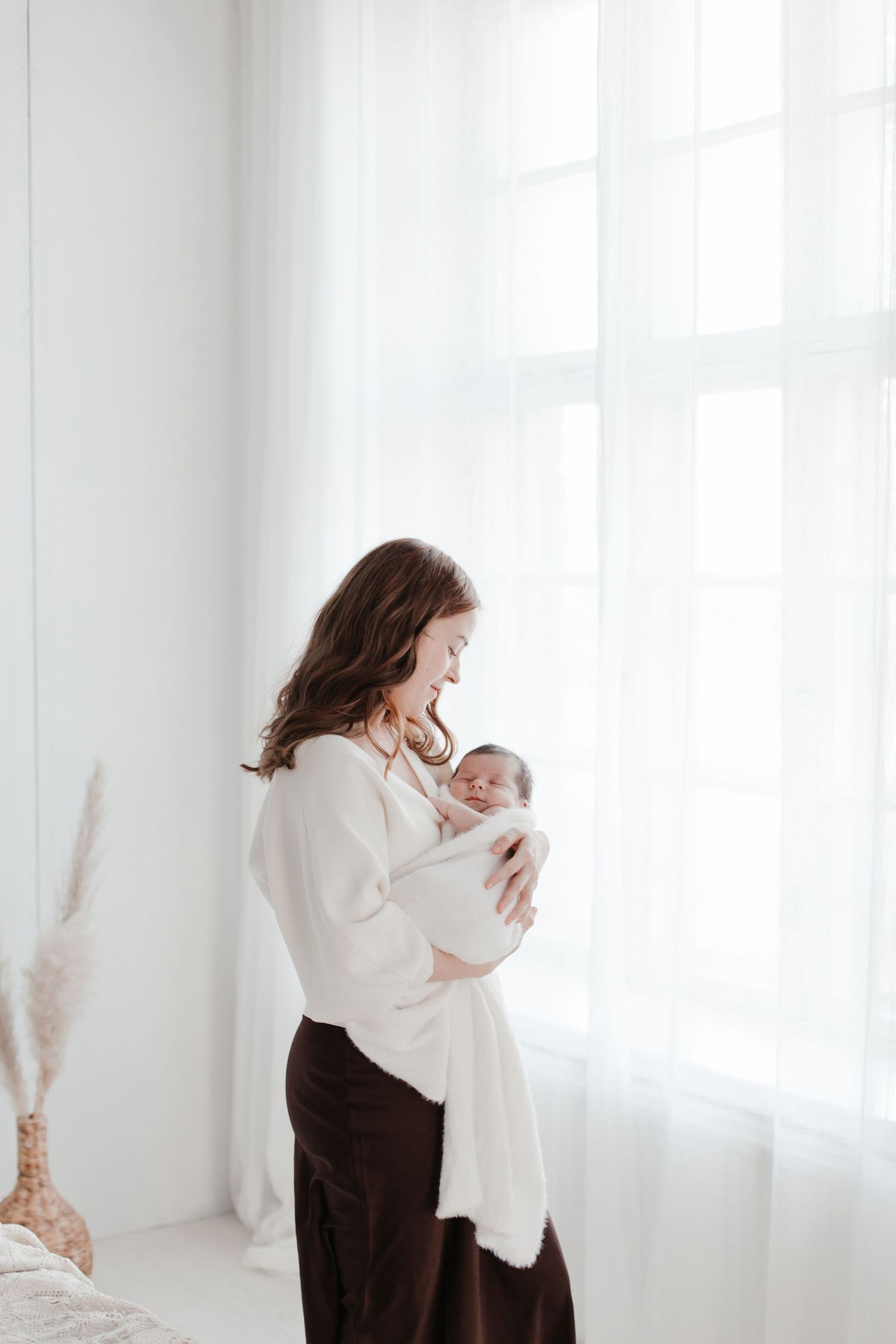 Mother holding baby in bright white room with natural window light.