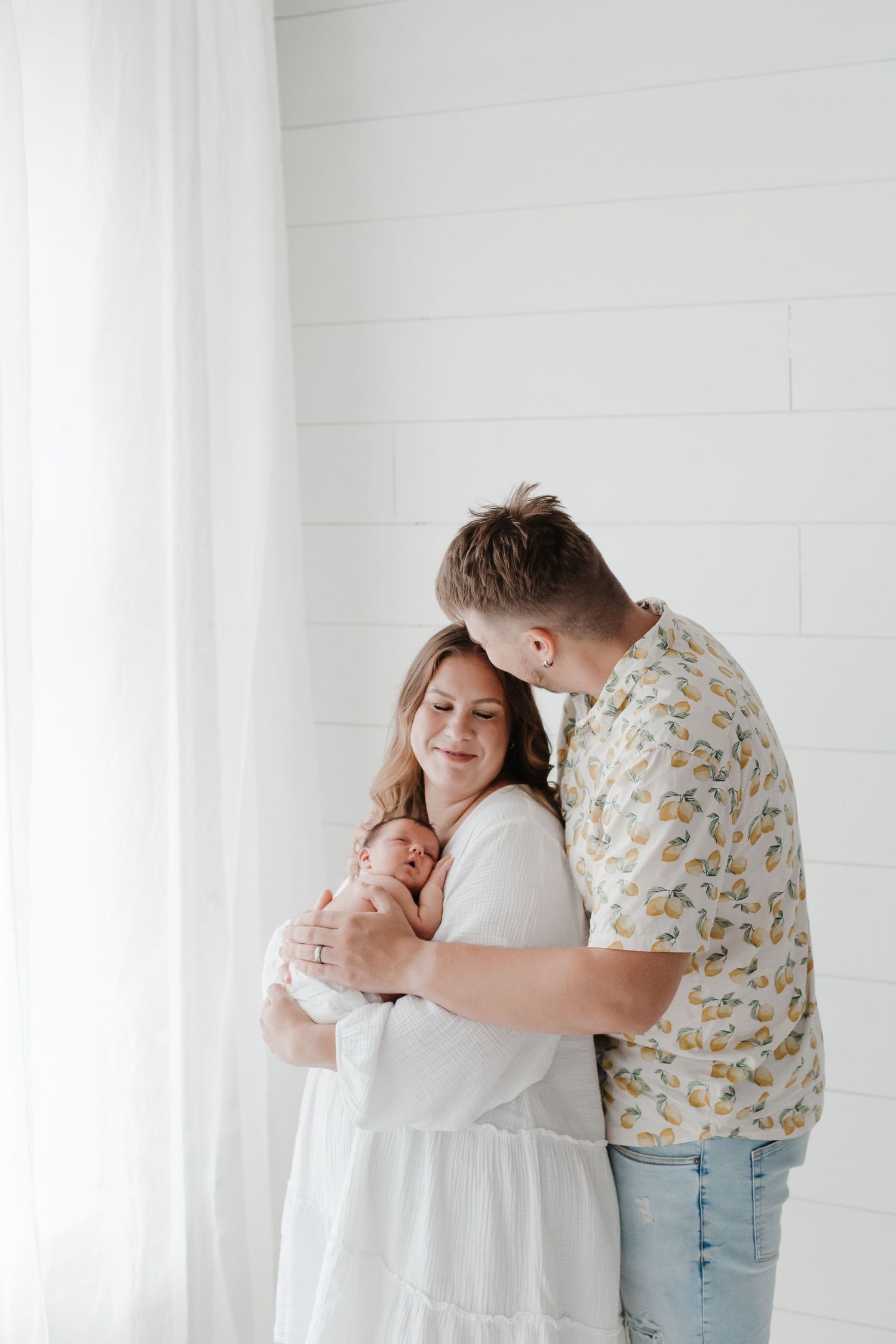 A loving family moment captured against white shiplap walls as they cuddle their newborn.