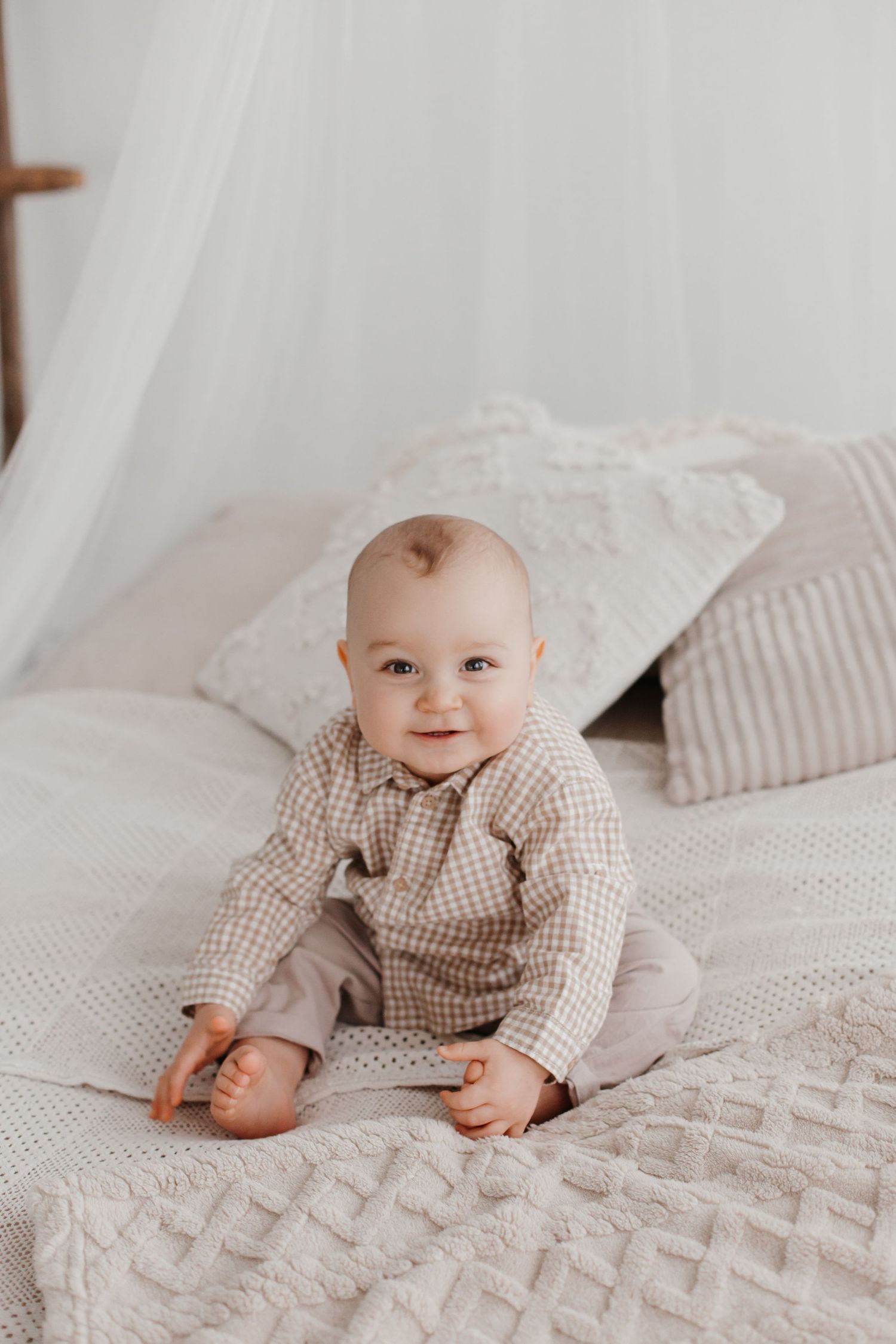 Baby in gingham shirt playing on white textured bedspread.