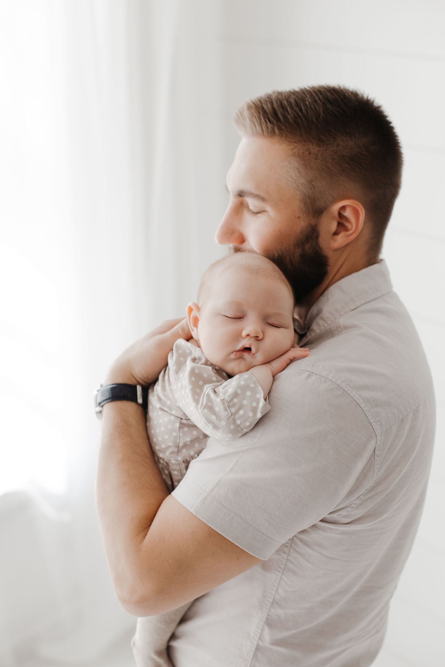 Tender moment between parent and sleeping baby in bright, minimal setting.